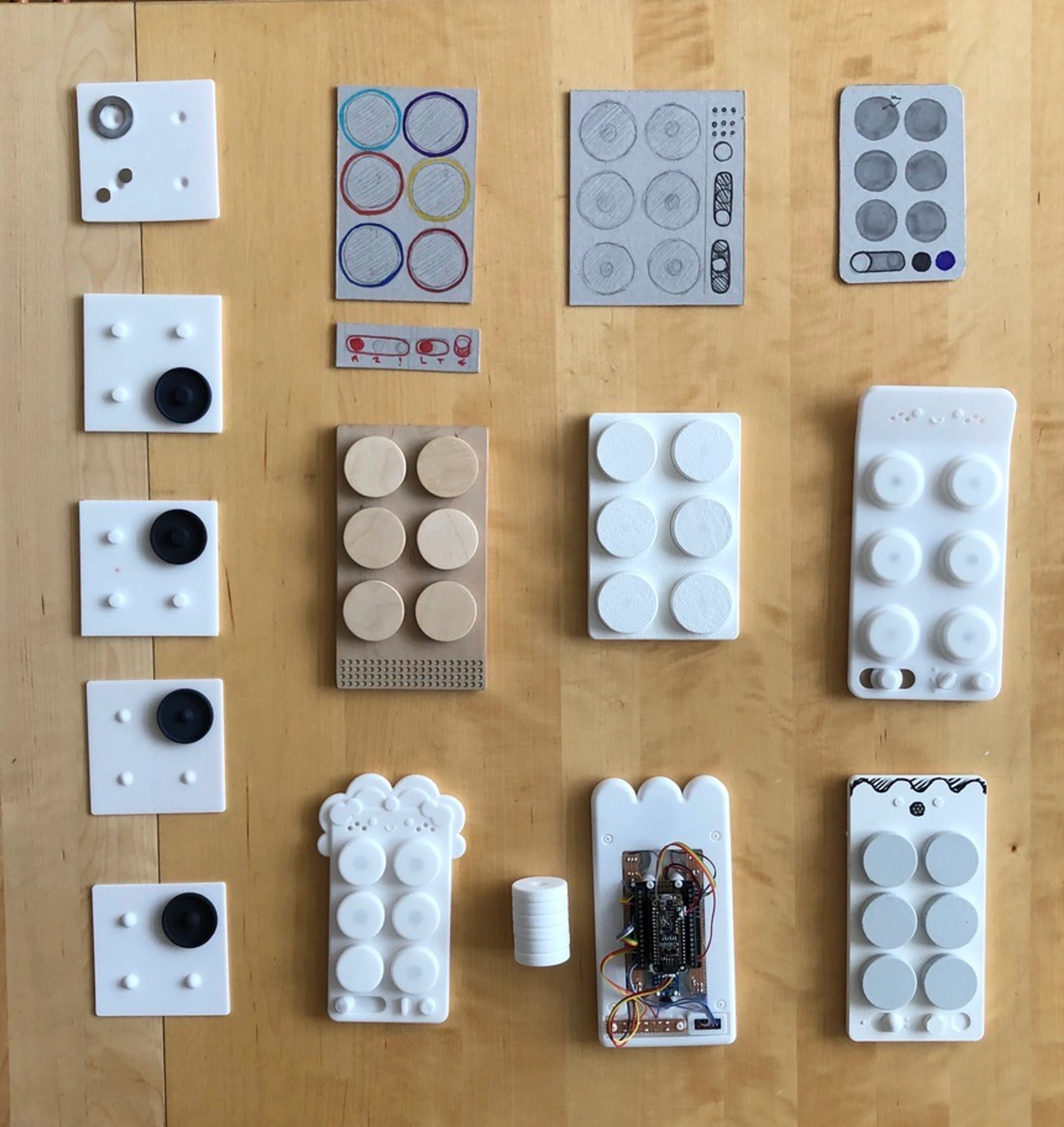 Printed button and interface studies laid out on plywood beside their sketches