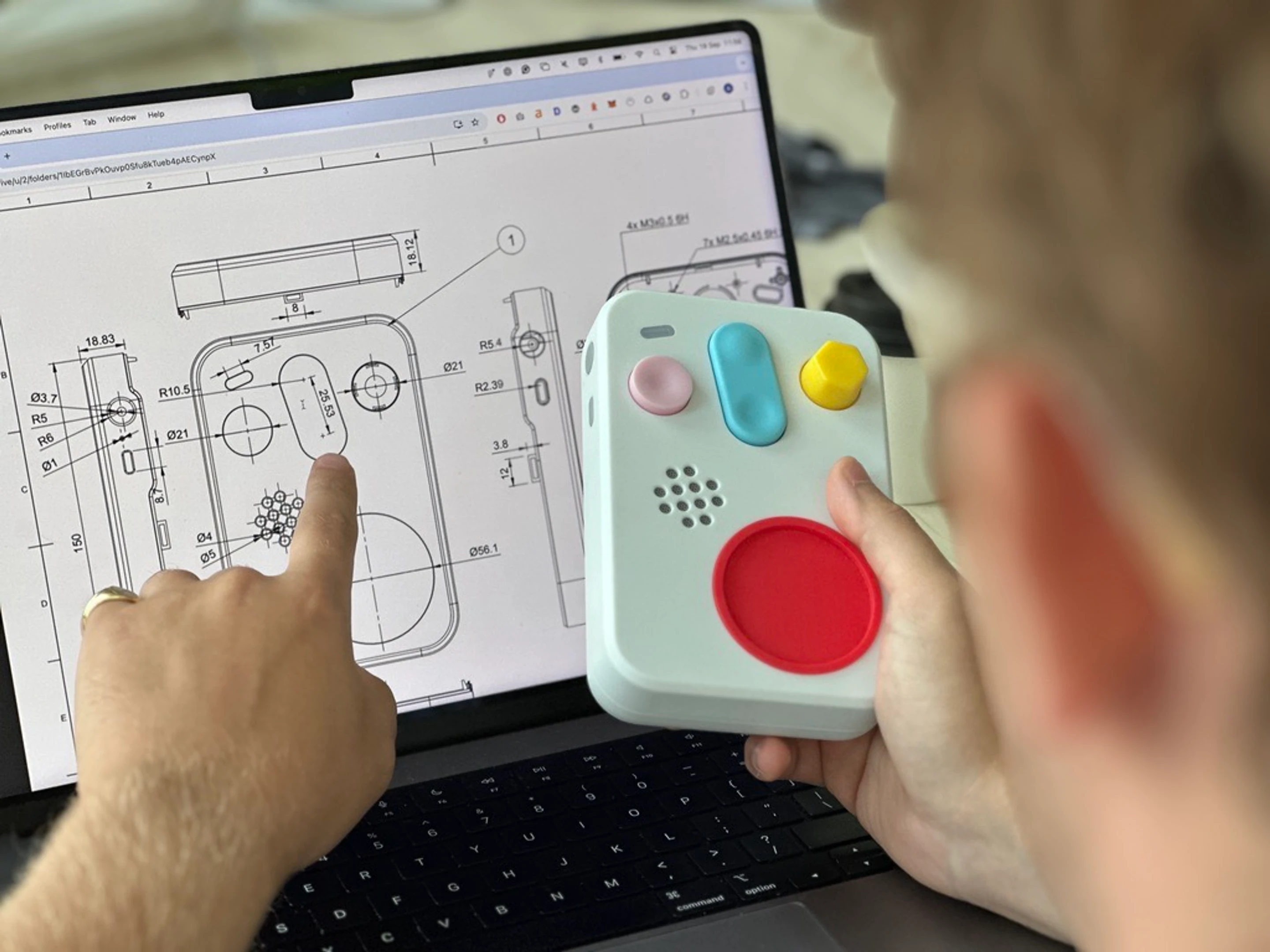 A printed handheld held up against its own CAD drawing on screen