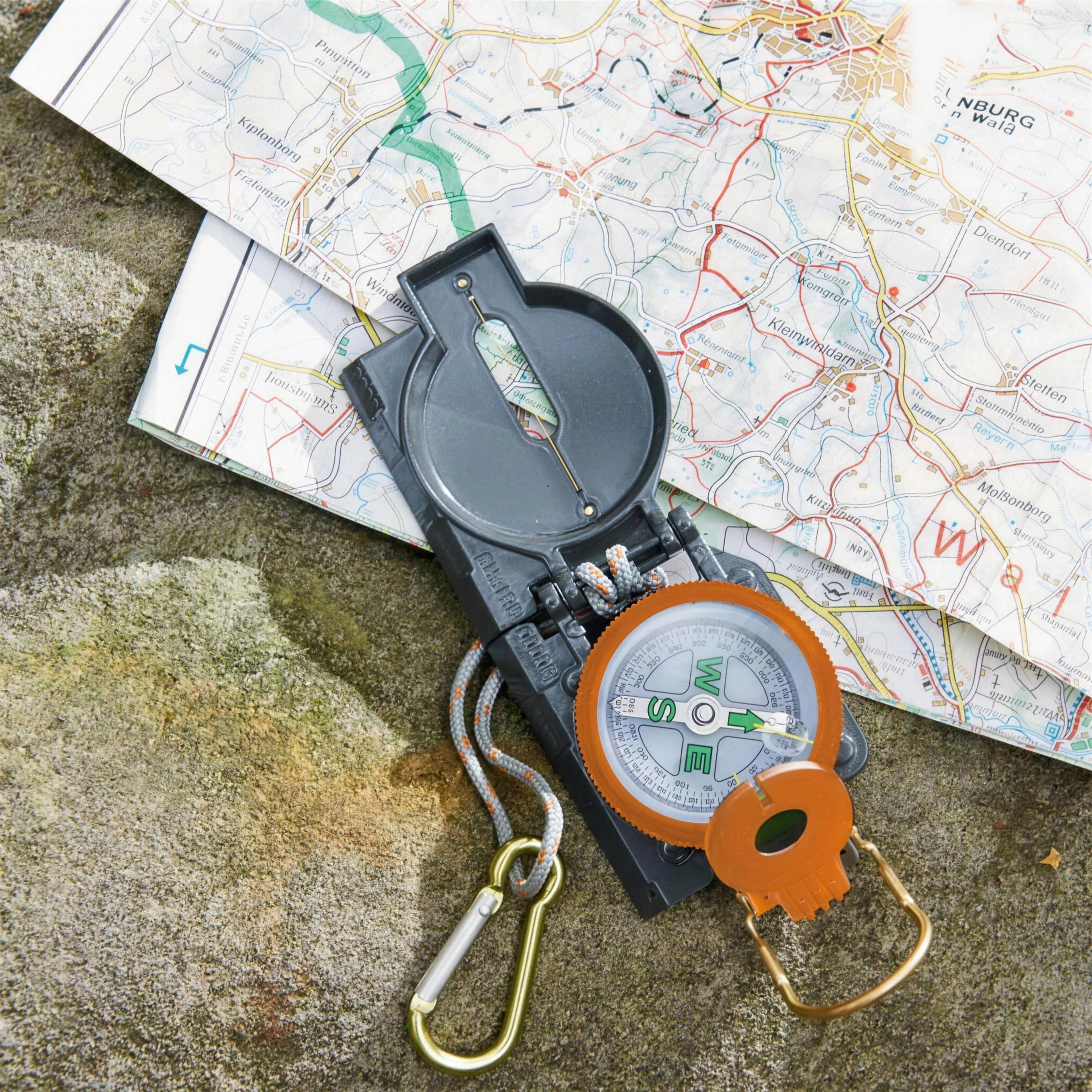 A compass resting on a folded walking map, on a sunlit rock