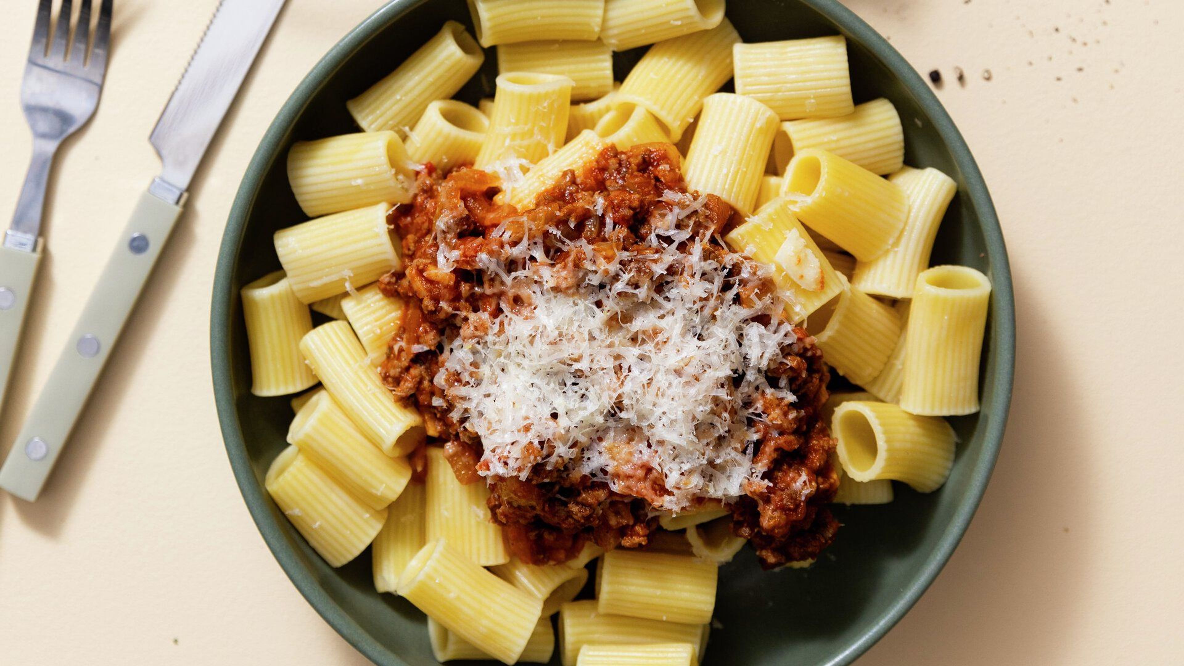 Pastaa ja lihakastiketta, päällä juustoraastetta. Valmistettu lautasella.