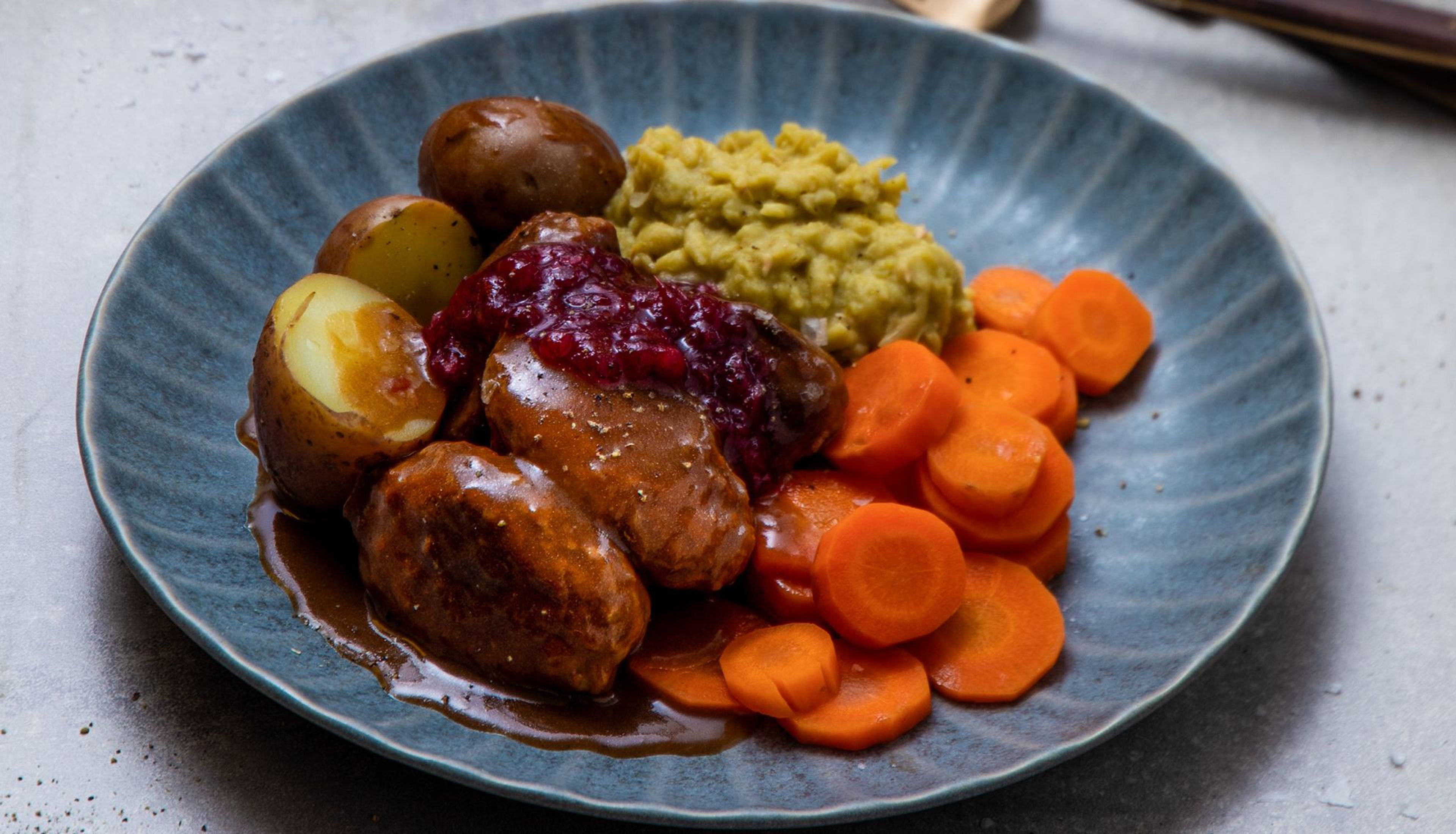 Kjøttkaker med brun saus, erter, gulrøtter, poteter og tyttebær.