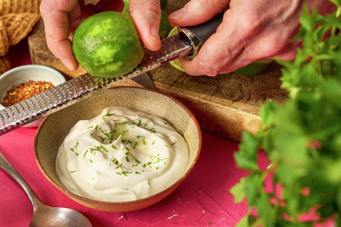Skål med limeyoghurt, hånd som river limeskall på rivjern.