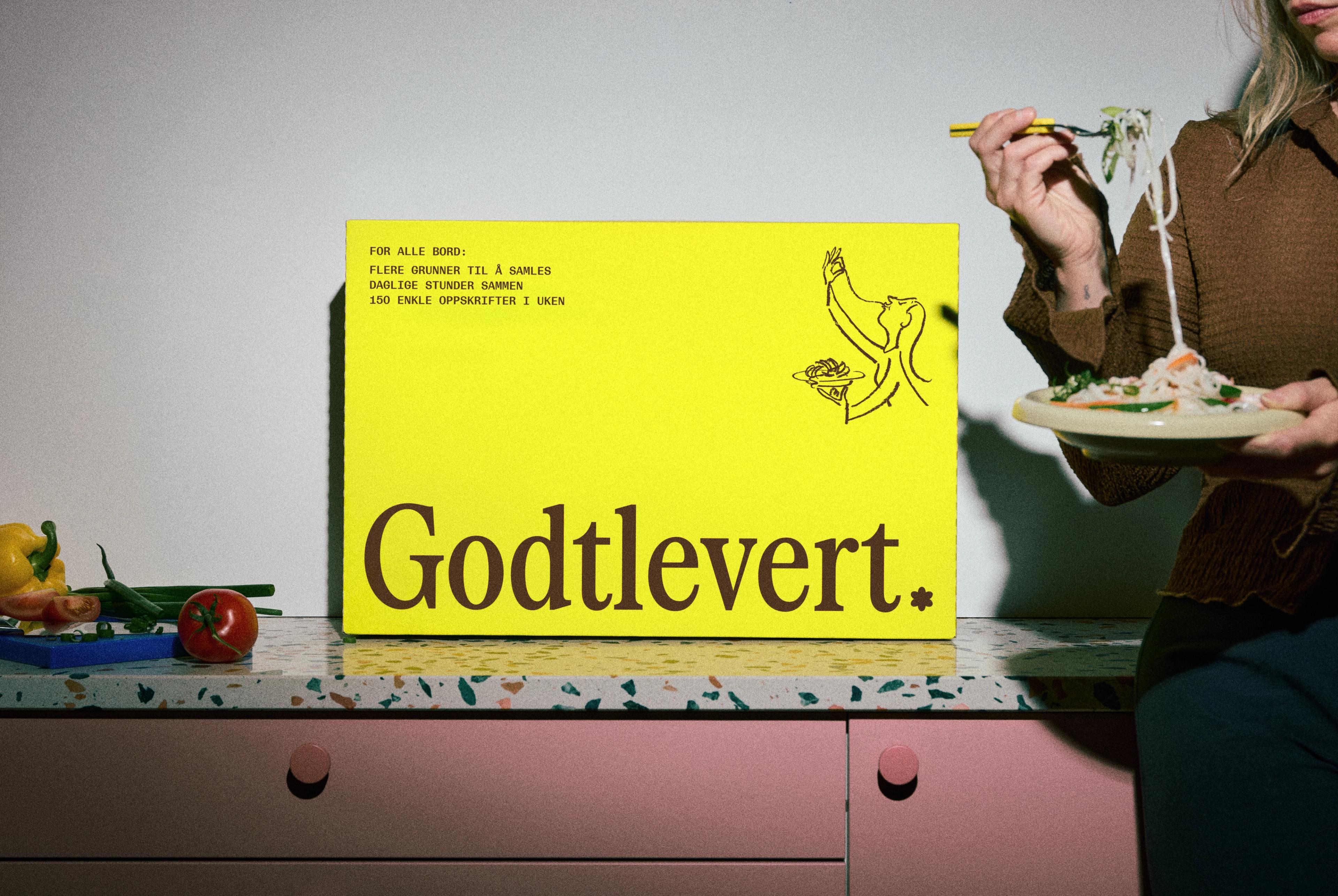 En kvinne som holder en tallerken med mat foran en gul eske med teksten "Godtlevert".