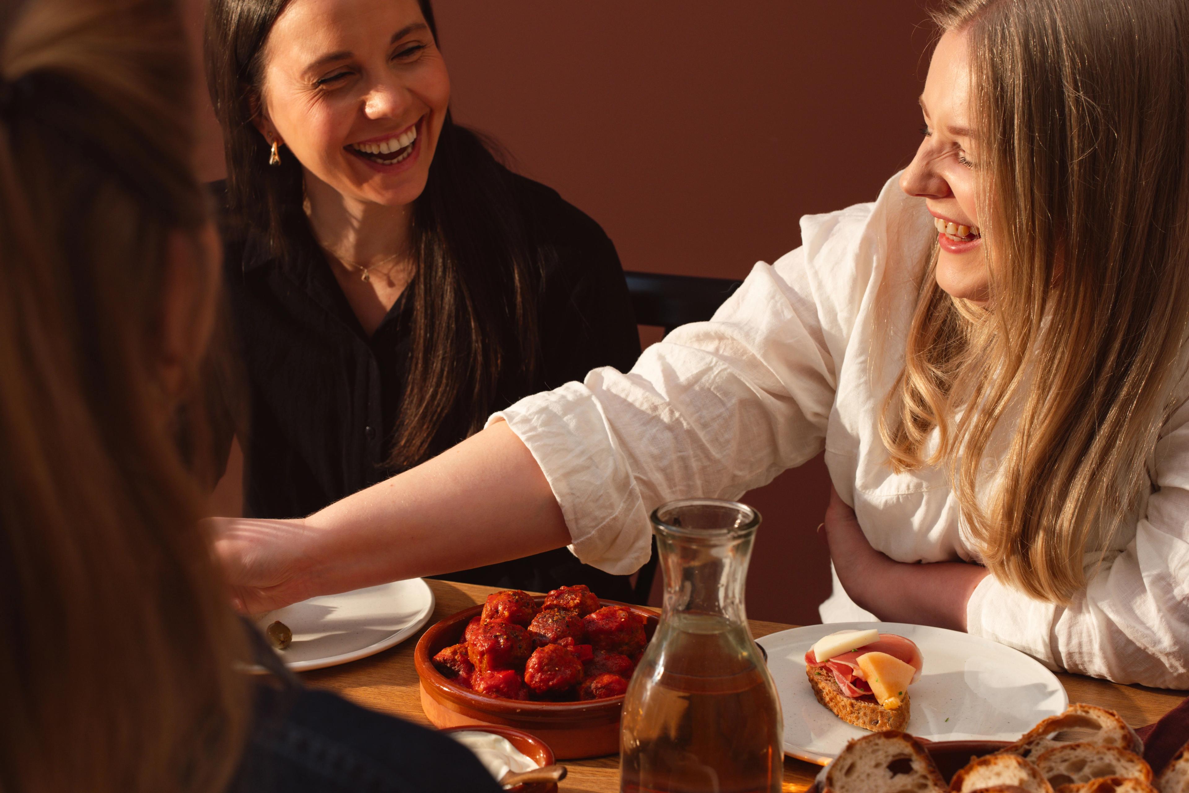 Skrattende kvinner rundt et dekket middagsbord