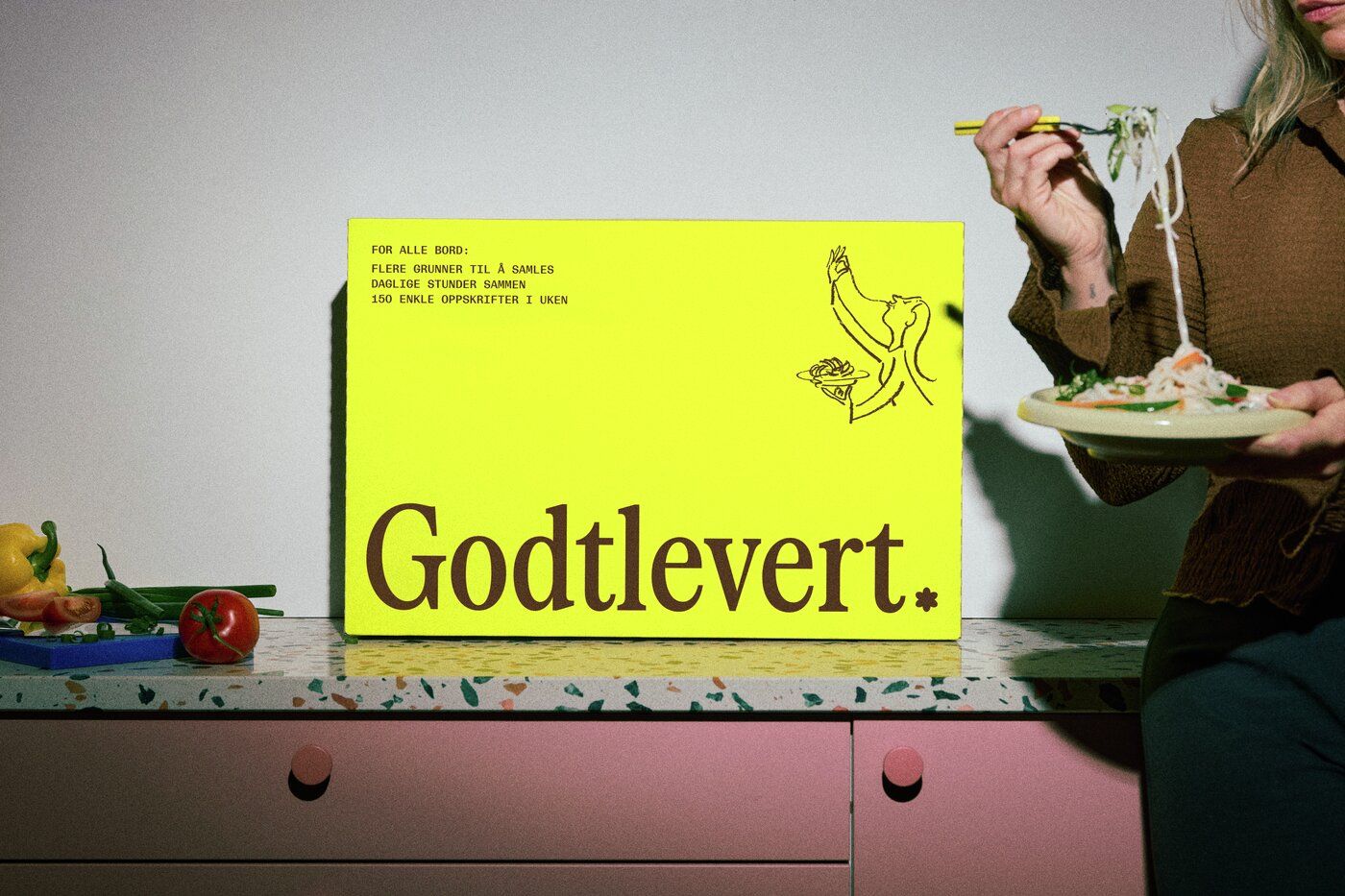 En person serverer pasta fra en stor grønnsakskasse på en benk.