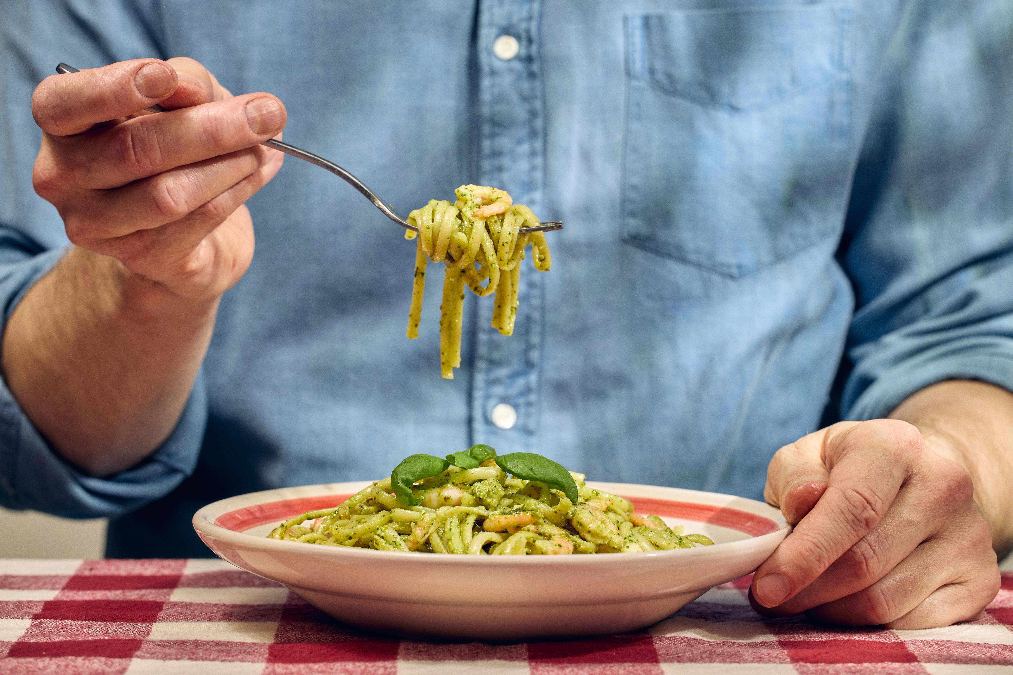 En mann spiser linguine med gaffel