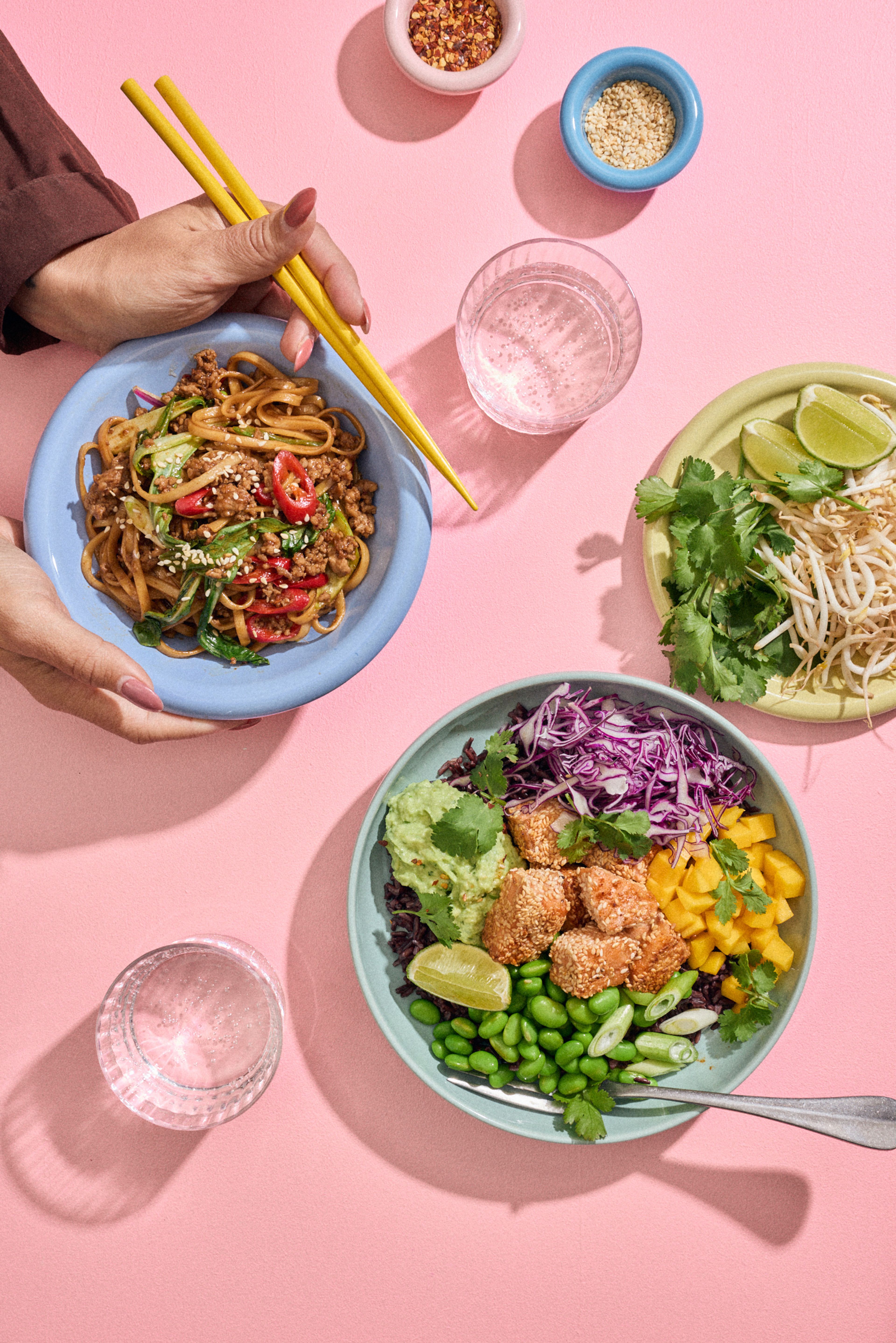 To skåler med nudler og laksebowl servert på et rosa bord