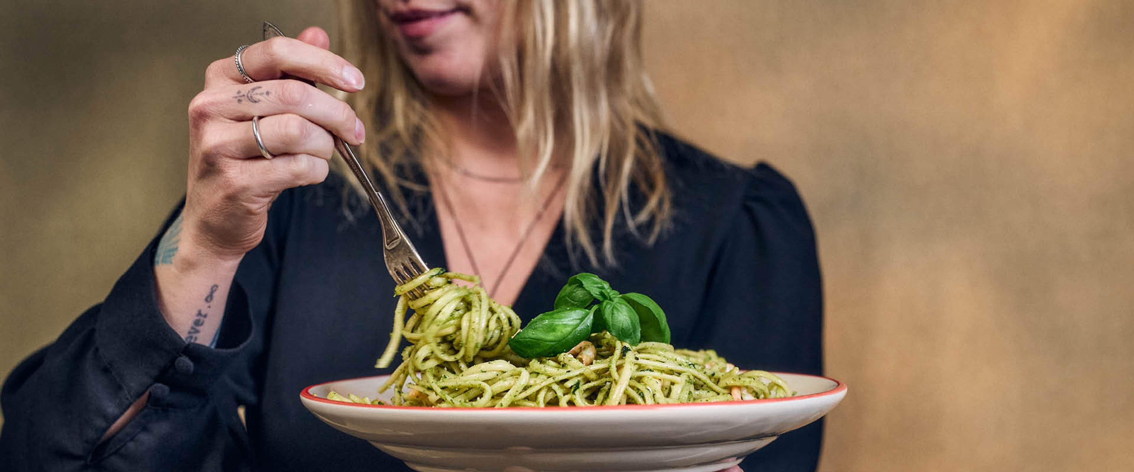 En person holder en tallerken spaghetti med pesto og snurrer opp pasta med en gaffel