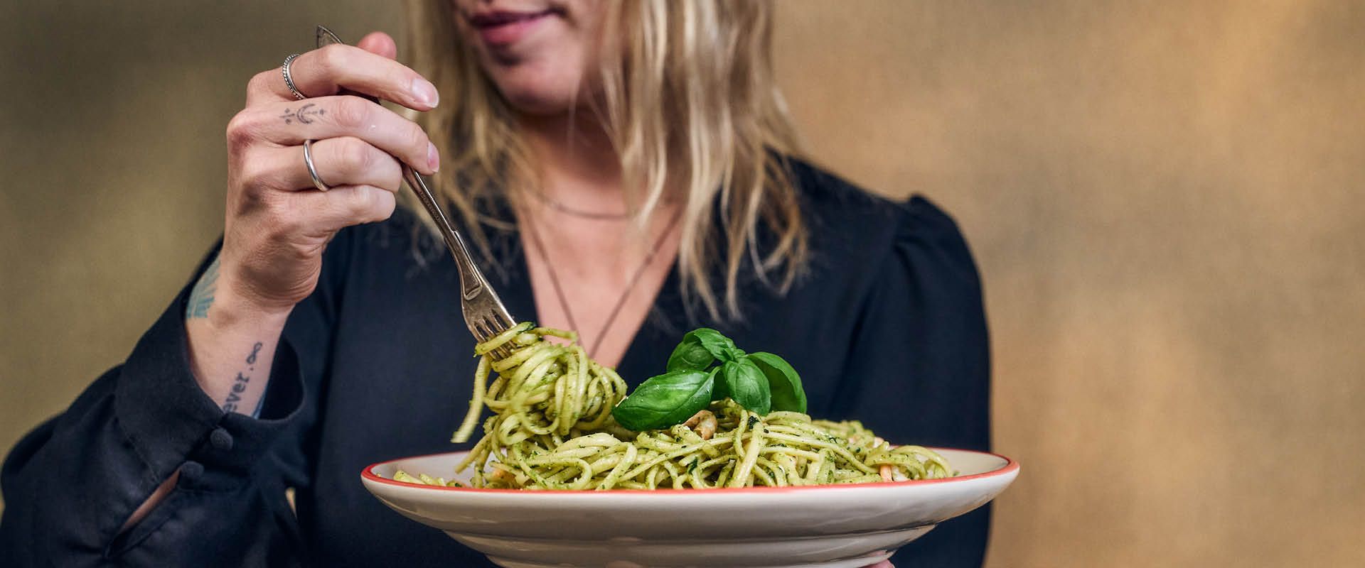 En person holder en tallerken spaghetti med pesto og snurrer opp pasta med en gaffel