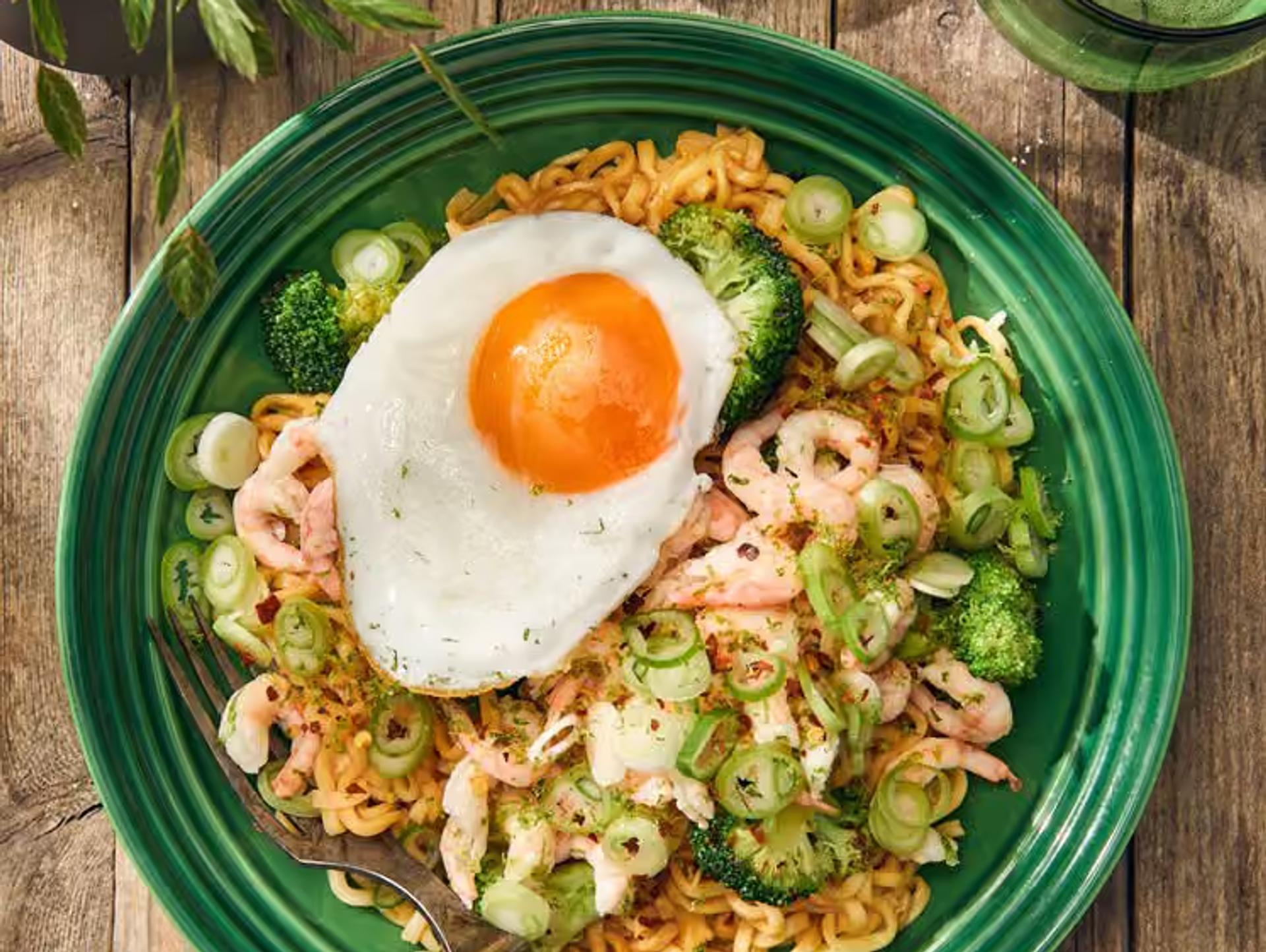 Nudlar med räkor, broccoli och ett stekt ägg, serverat på grön tallrik.