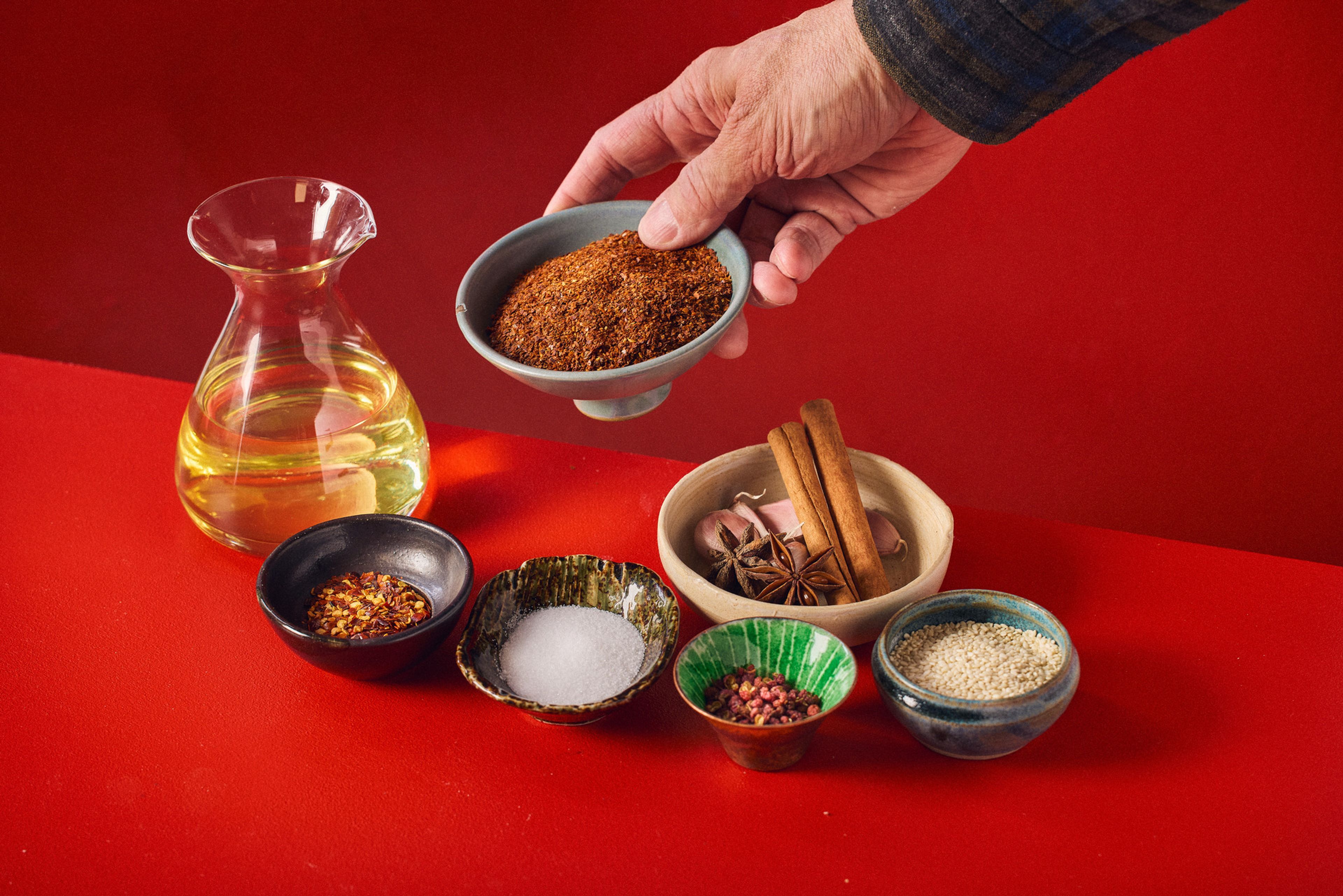 En kanna olja och små skålar med kryddor mot röd bakgrund