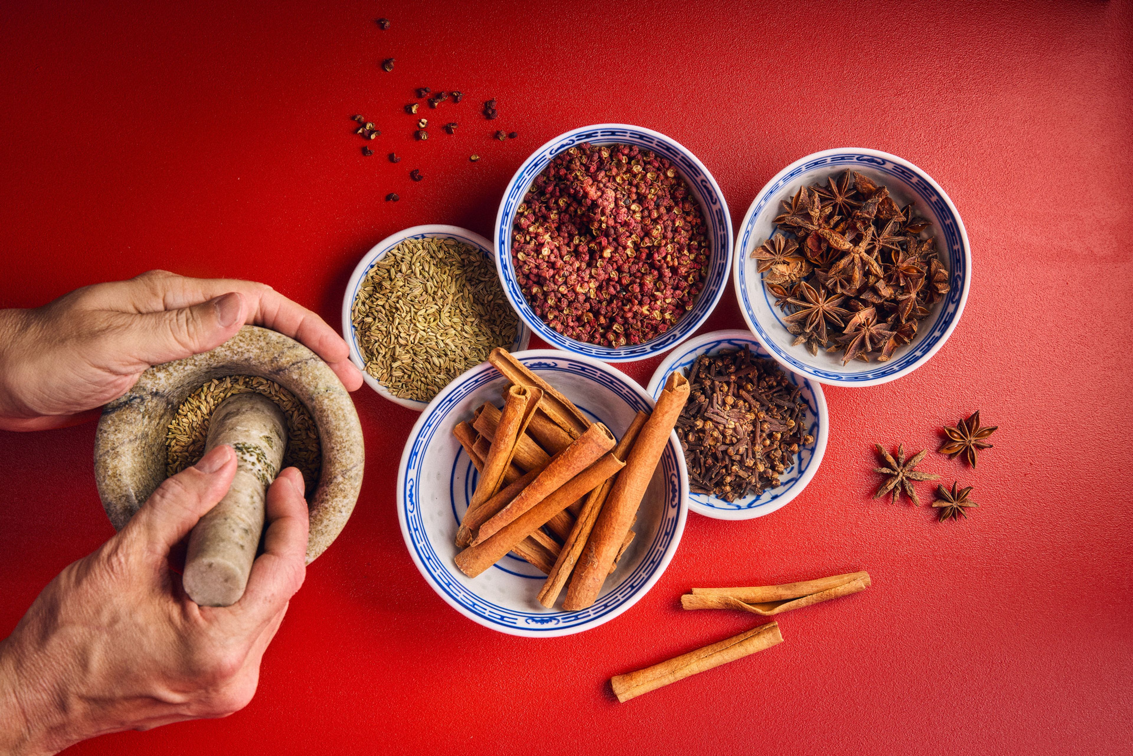 En mortel och flera kinesiska skålar med kryddor mot röd bakgrund