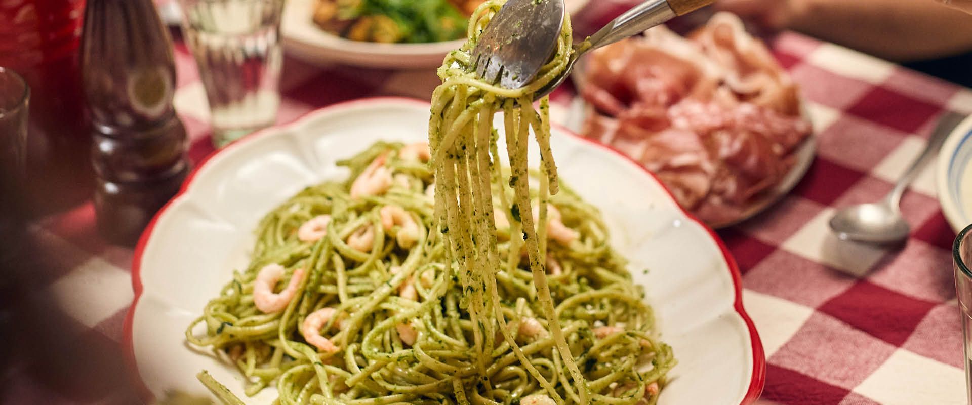 Spaghetti med grön pesto snurras upp på gaffel vid ett dukat middagsbord