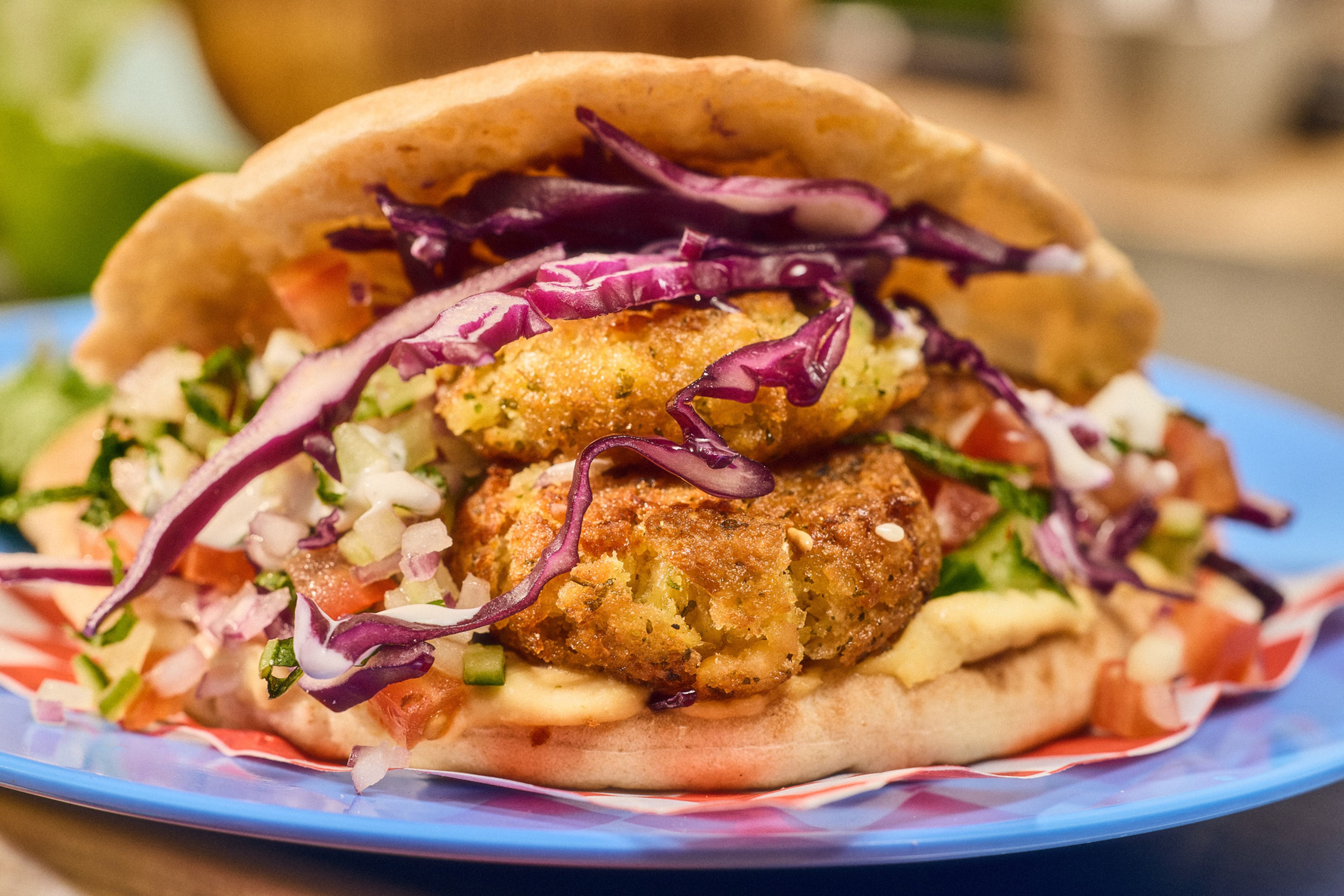 Falafel i pitabröd med myntasallad, yoghurtsås och hummus, serverat på en blå plasttallrik.