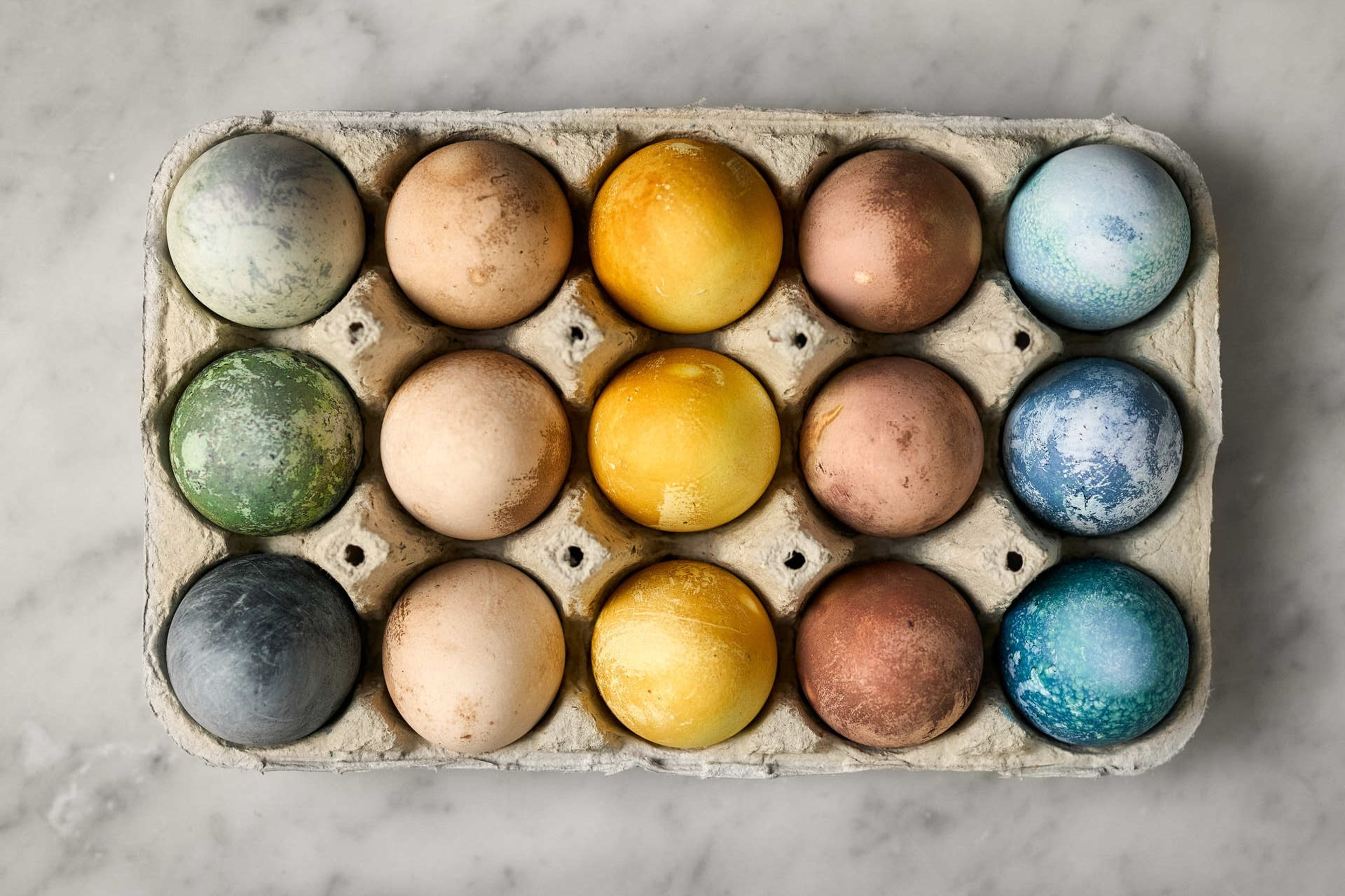 Ägg i en äggkartong fotograferad uppifrån. Äggen är gröna, bruna, blå, gula och svarta.