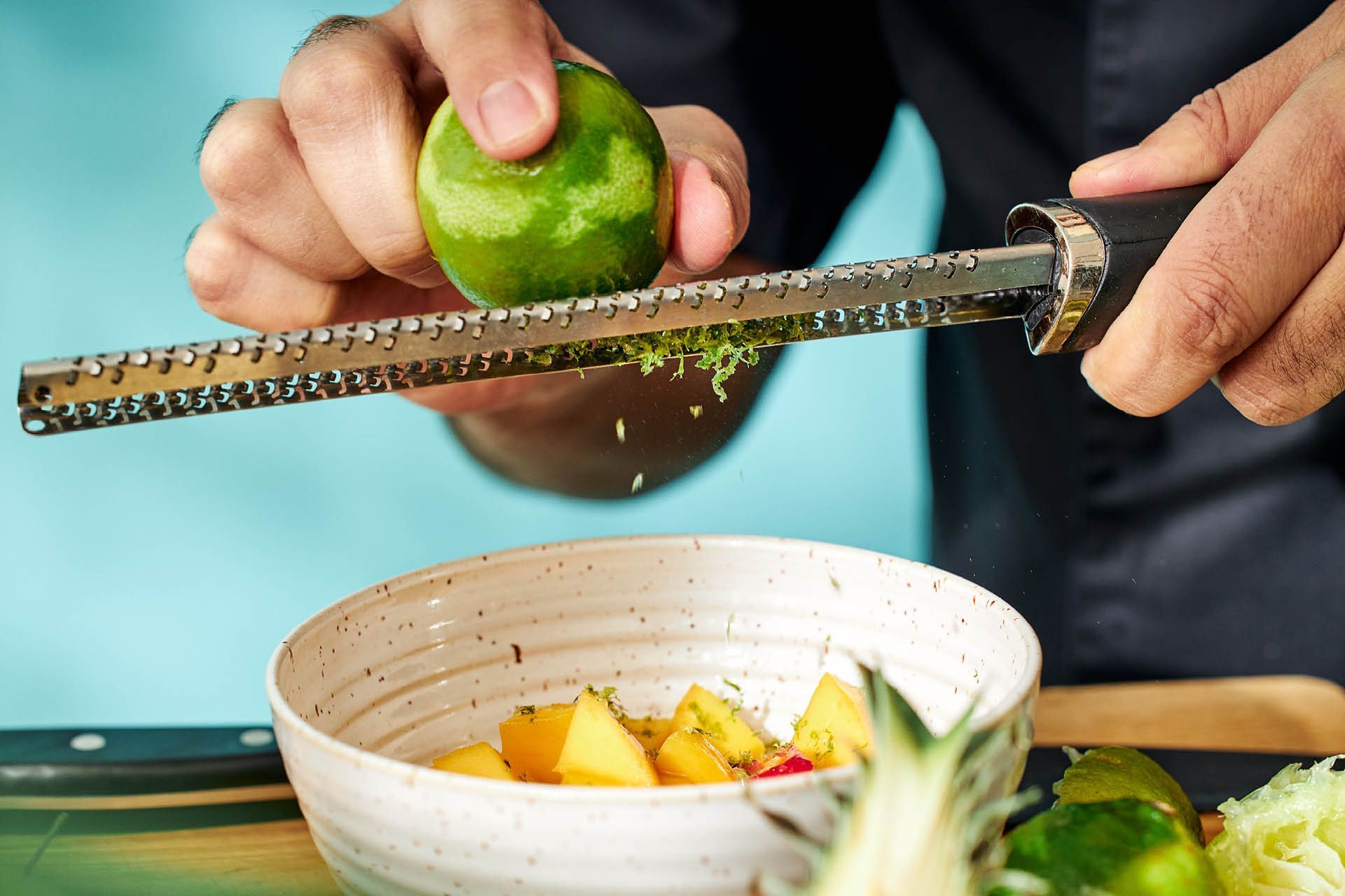 Händer som river limefrukt över en skål med salsa