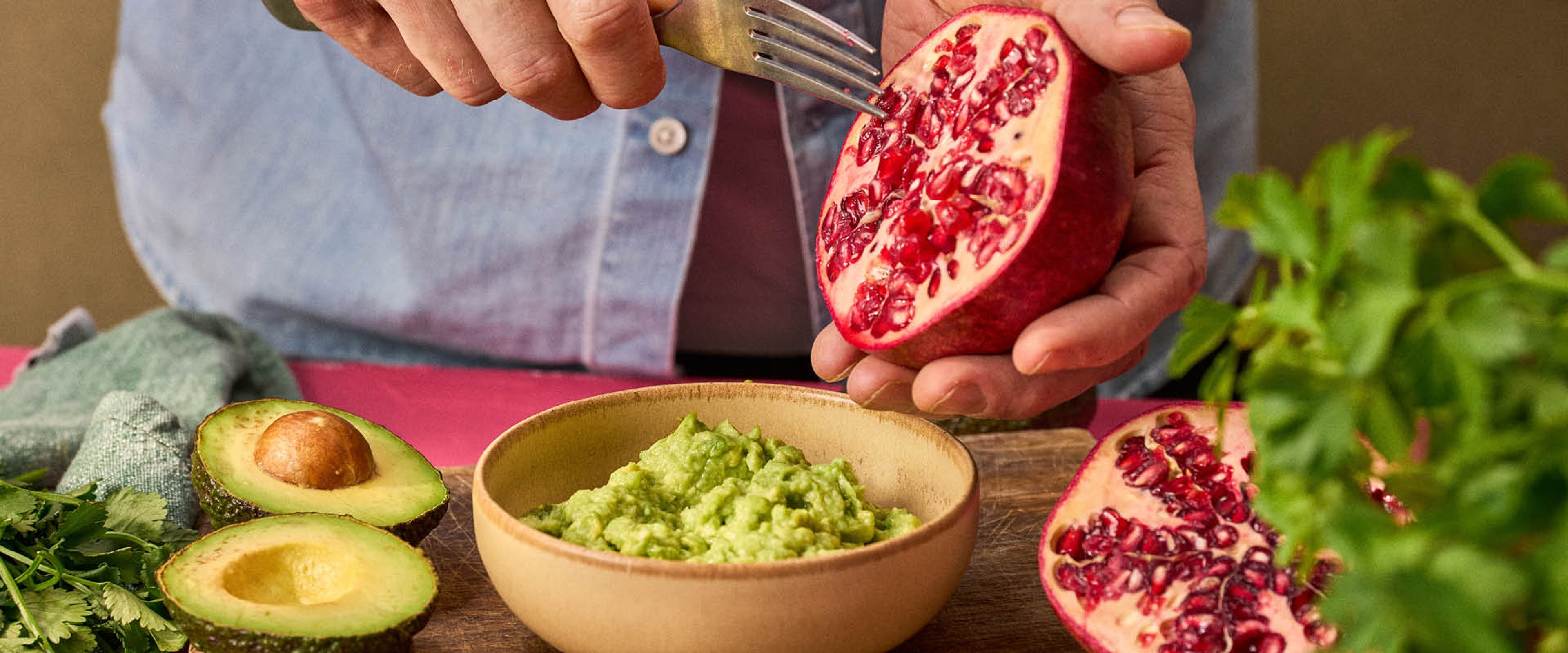 En skål med guacamole, gaffel som skrapar ur kärnor ur granatäpple