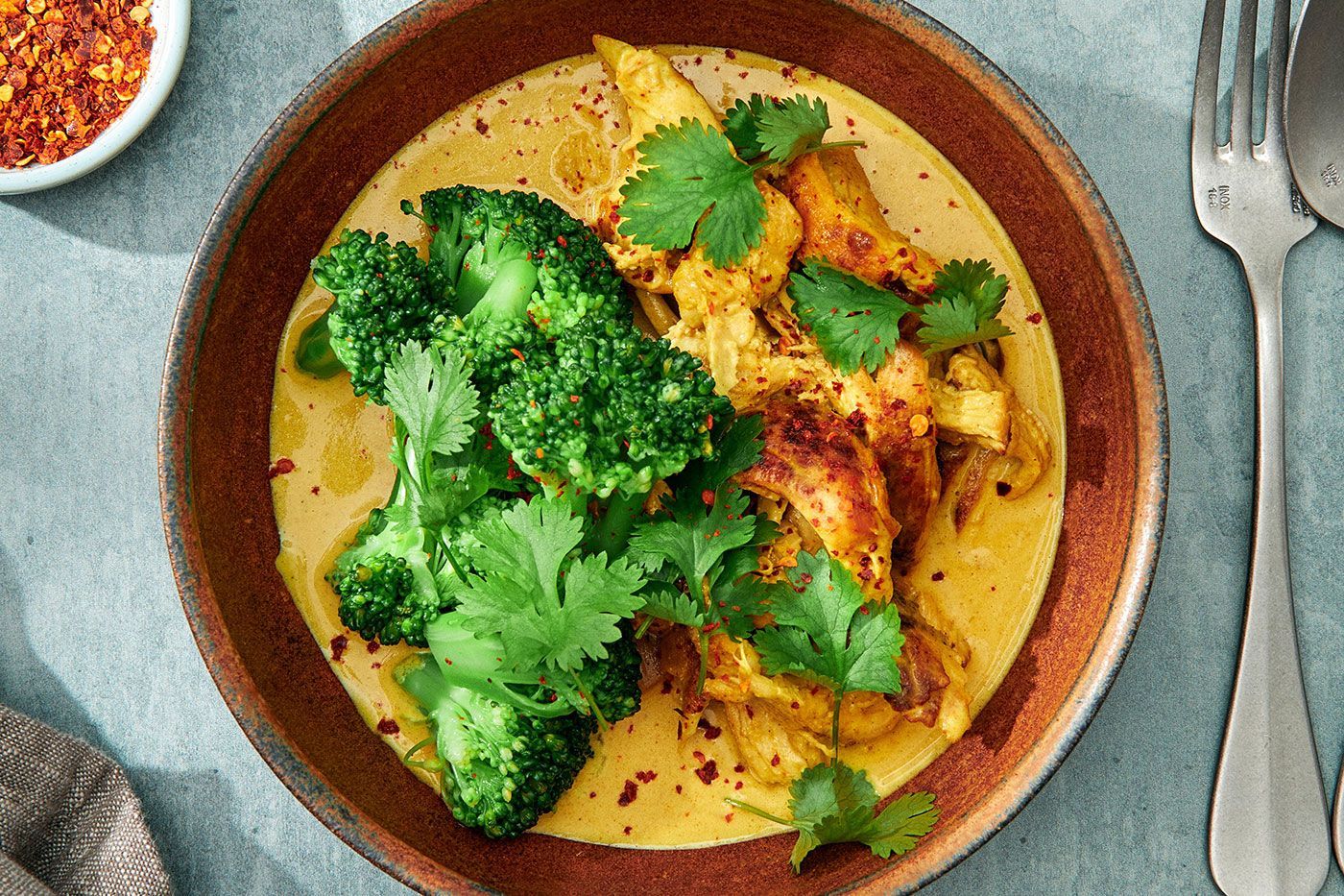 En djup tallrik med en gul kycklingcurry toppad med broccoli
