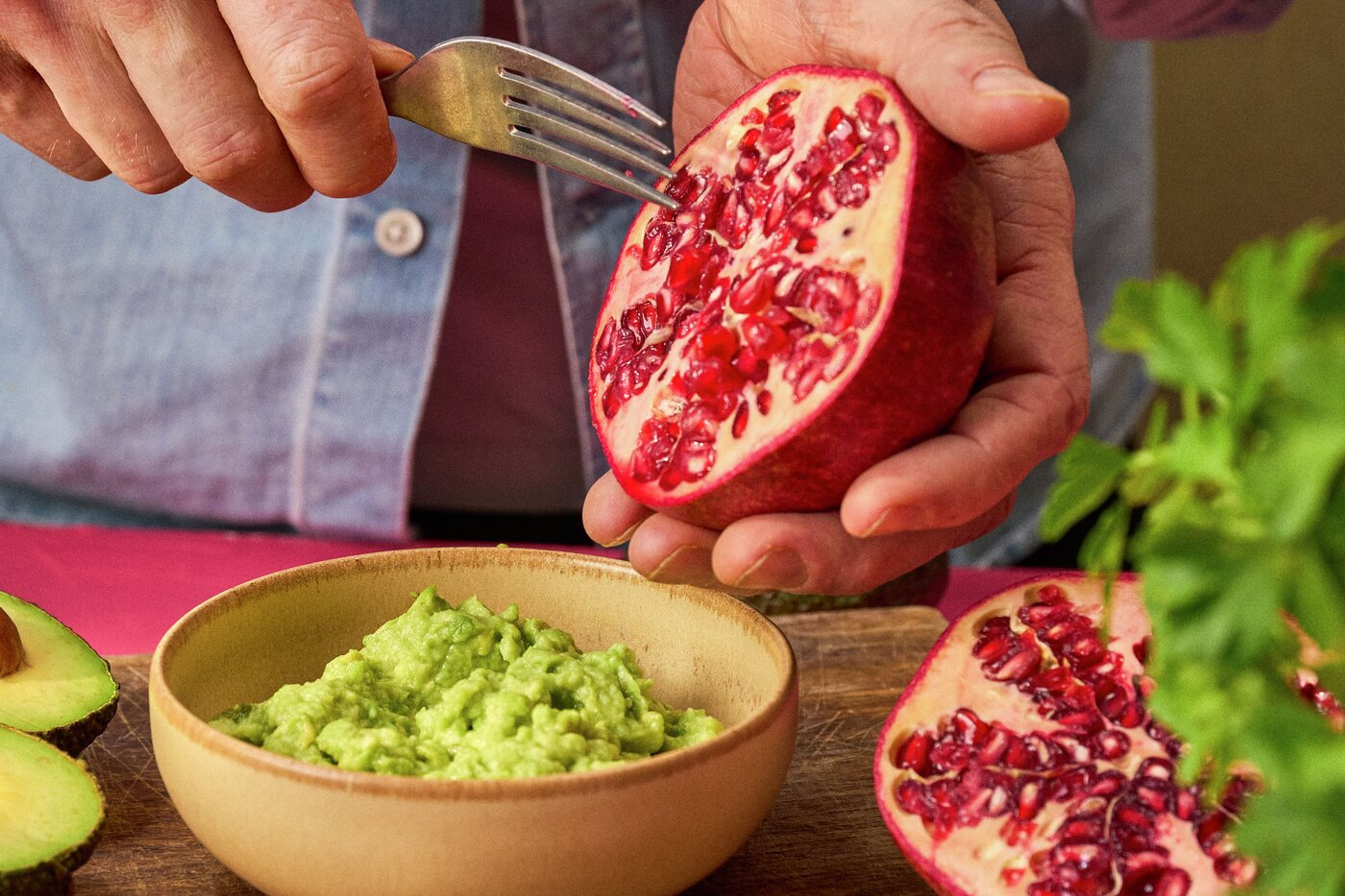 En skål med guacamole och gaffel som skrapar ur granatäpplekärnor
