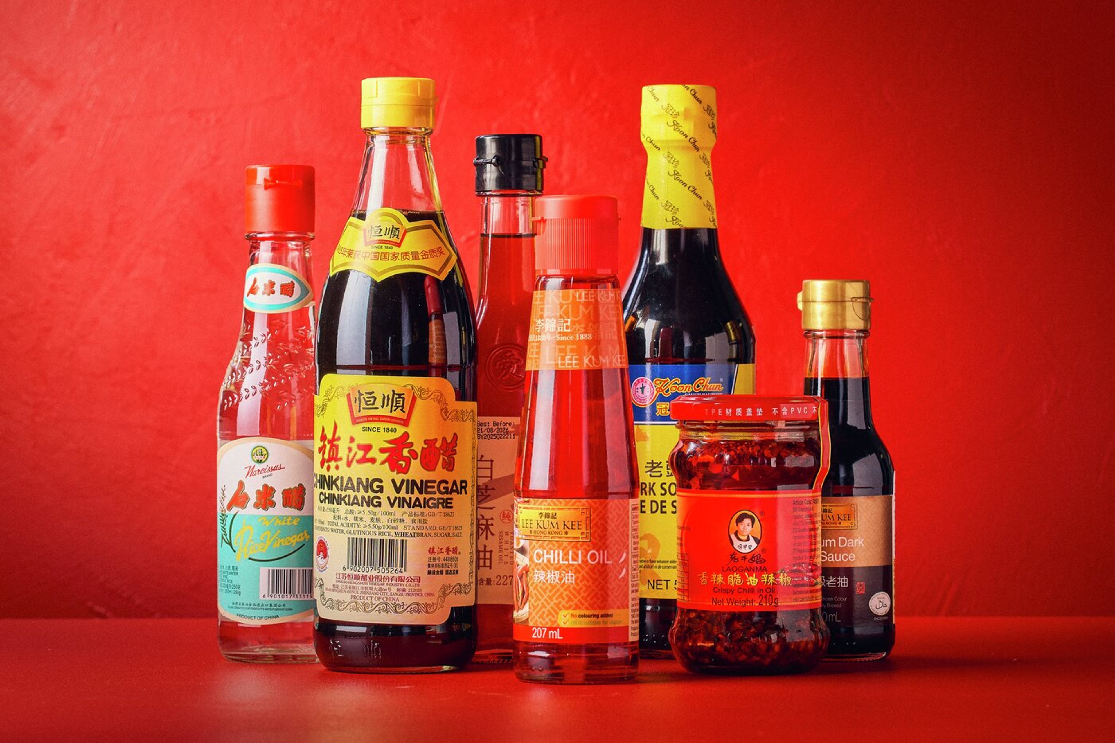 Färgglada flaskor och burkar med kinesiska smaksättare som soja och sesamolja, mot röd bakgrund