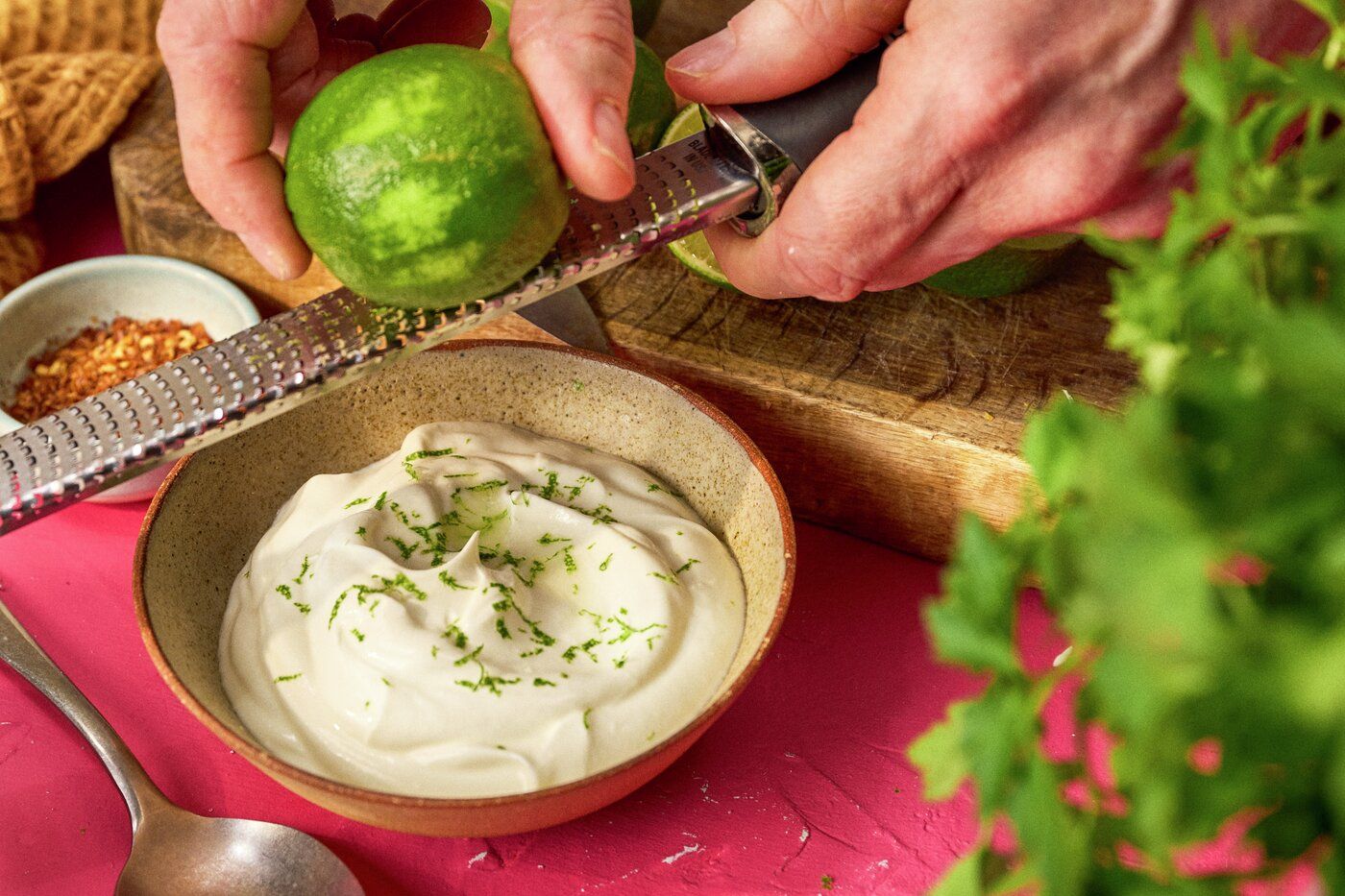 Skål med limeyoghurt, hand som river limeskal på rivjärn.