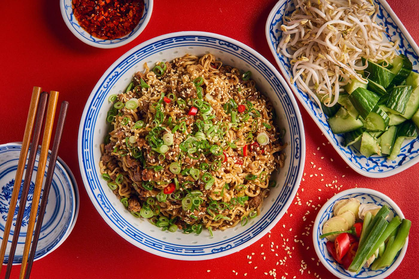 En skål med nudelwok med svinekød, chili, hvidløg og bønnespirer mod rød baggrund