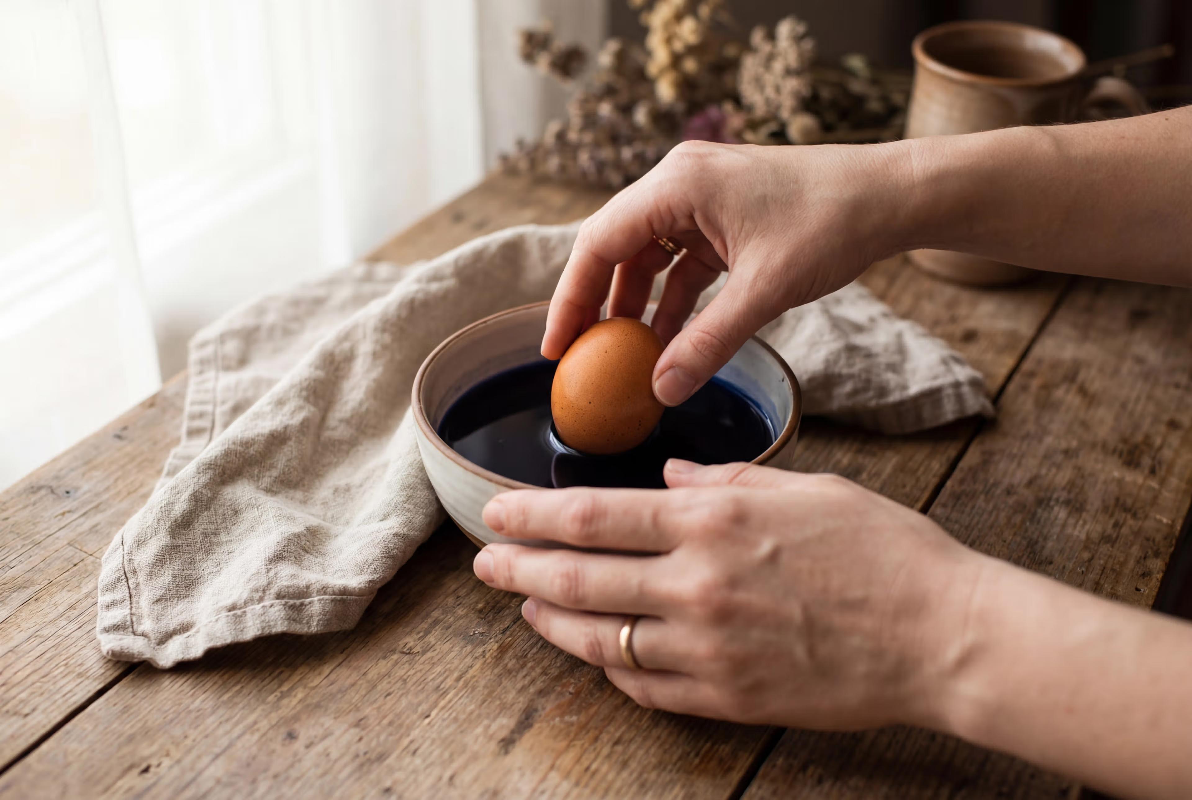 En hånd, der løfter et æg op af et farvebad.