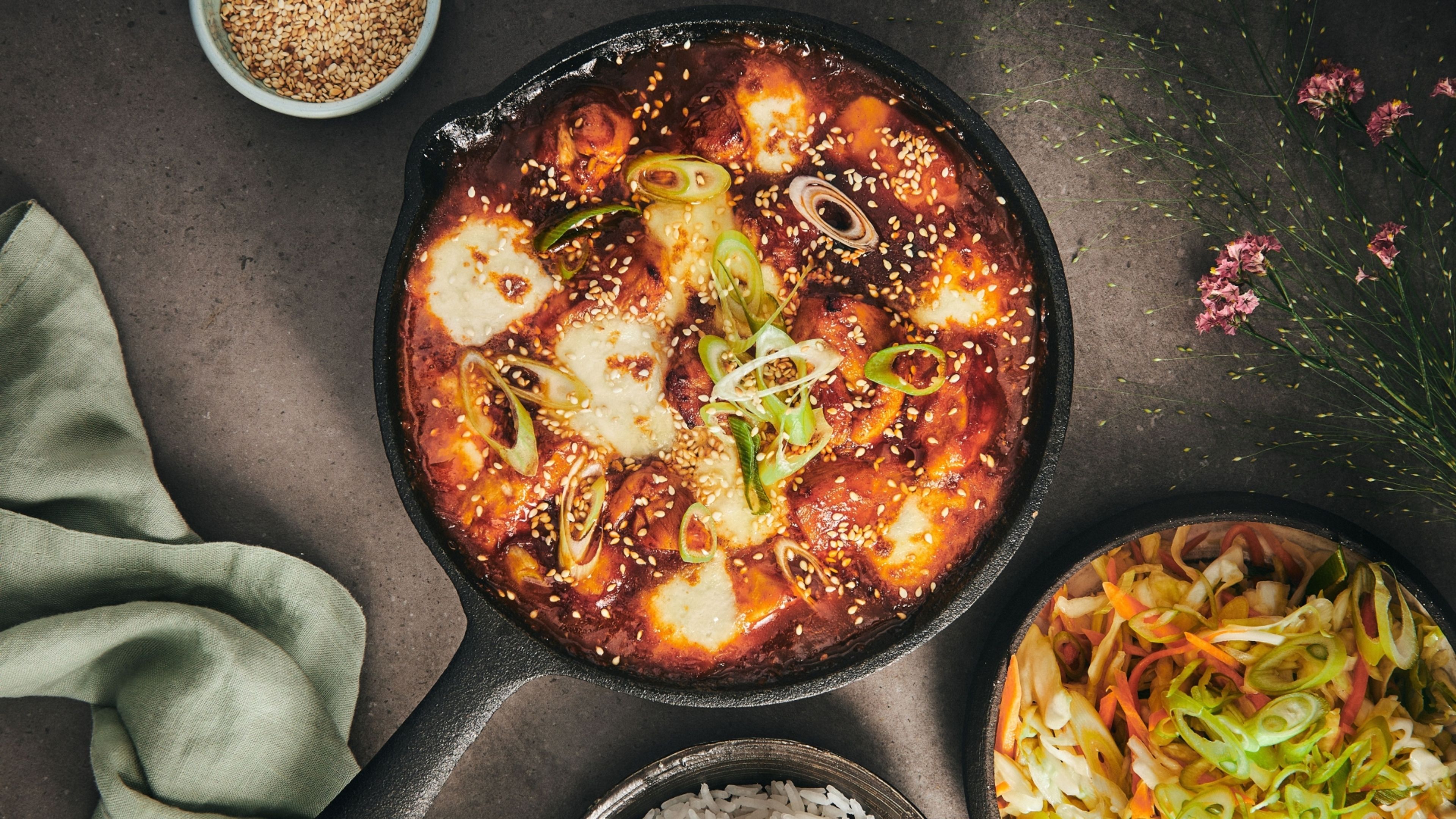 På billedet ses et herligt eksempel på en traditionel koreansk ret: buldak – ildkylling med gochujang, mozzarella, sesamfrø og koreansk coleslaw. I retten bruges gochujang som en base for en velsmagende ingefærsauce, der giver kyllingen sin stærke og rige smag.