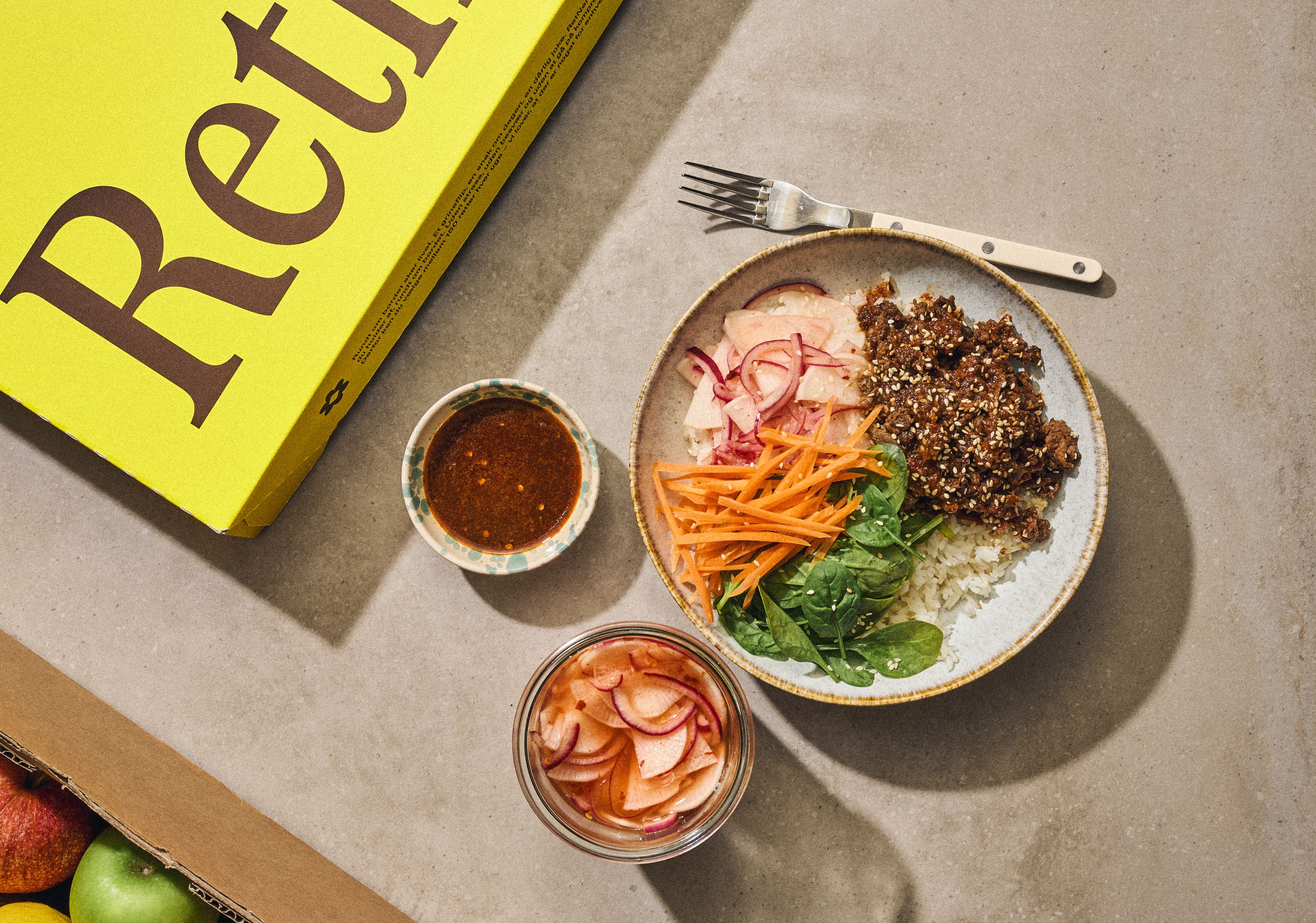 En tallerken med quinoa, grøntsager og sauce ved siden af en kasse med grøntsager.