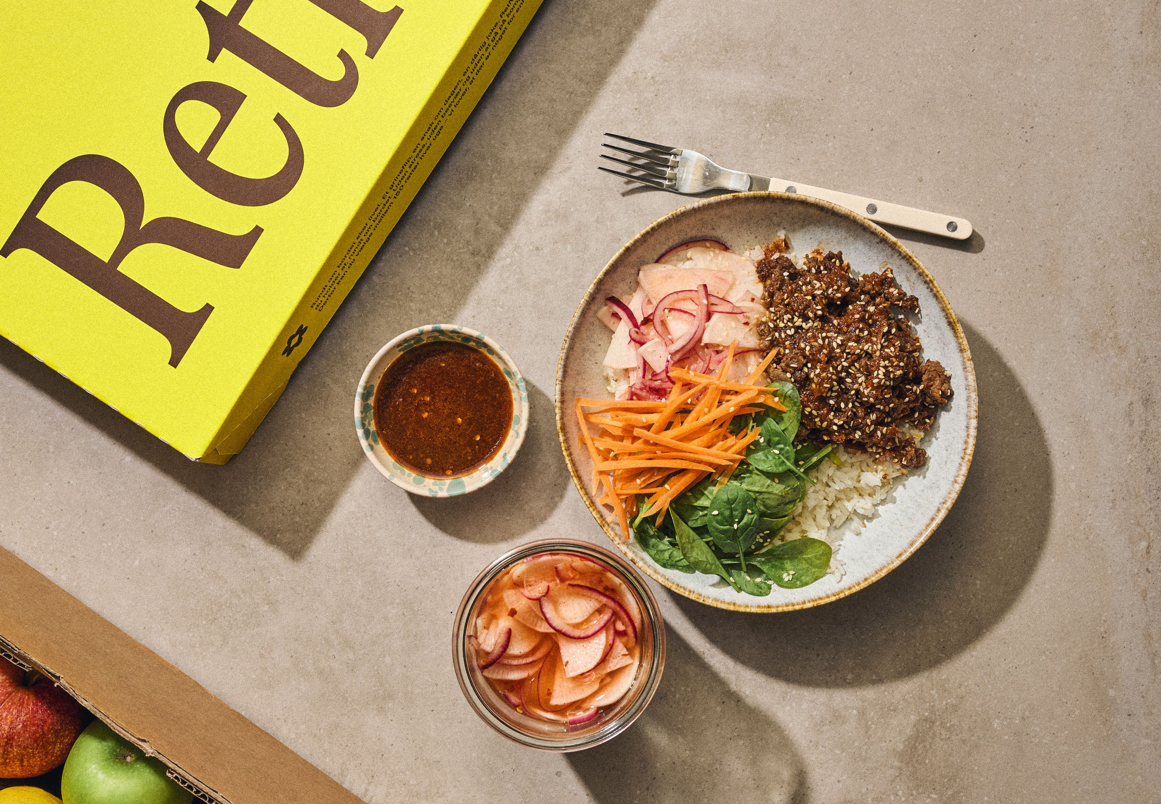 En tallerken med quinoa, grøntsager og sauce ved siden af en kasse med grøntsager.