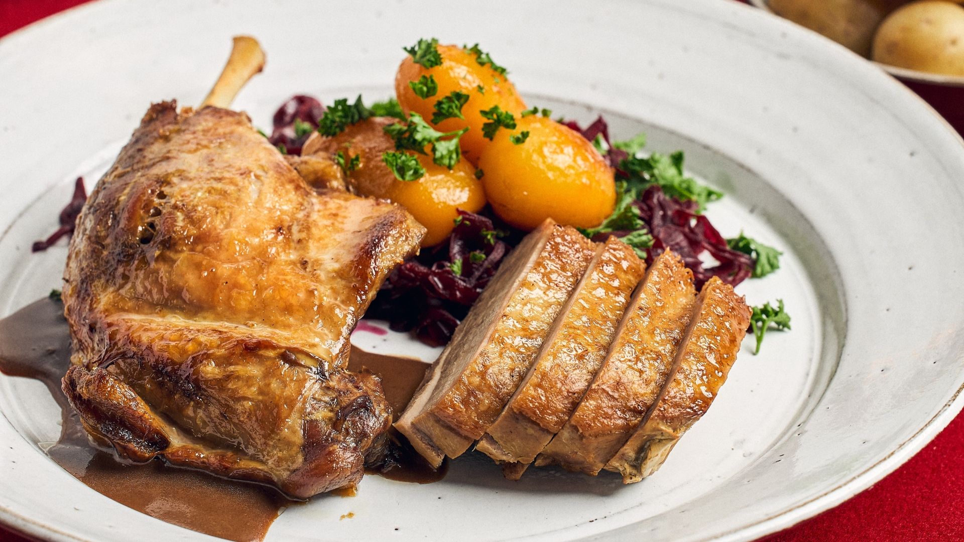 Confiteret andebryst og -lår, serveret med færdiglavet rødkål, brune kartofler, hvide kartofler, andesauce og persilledrys.