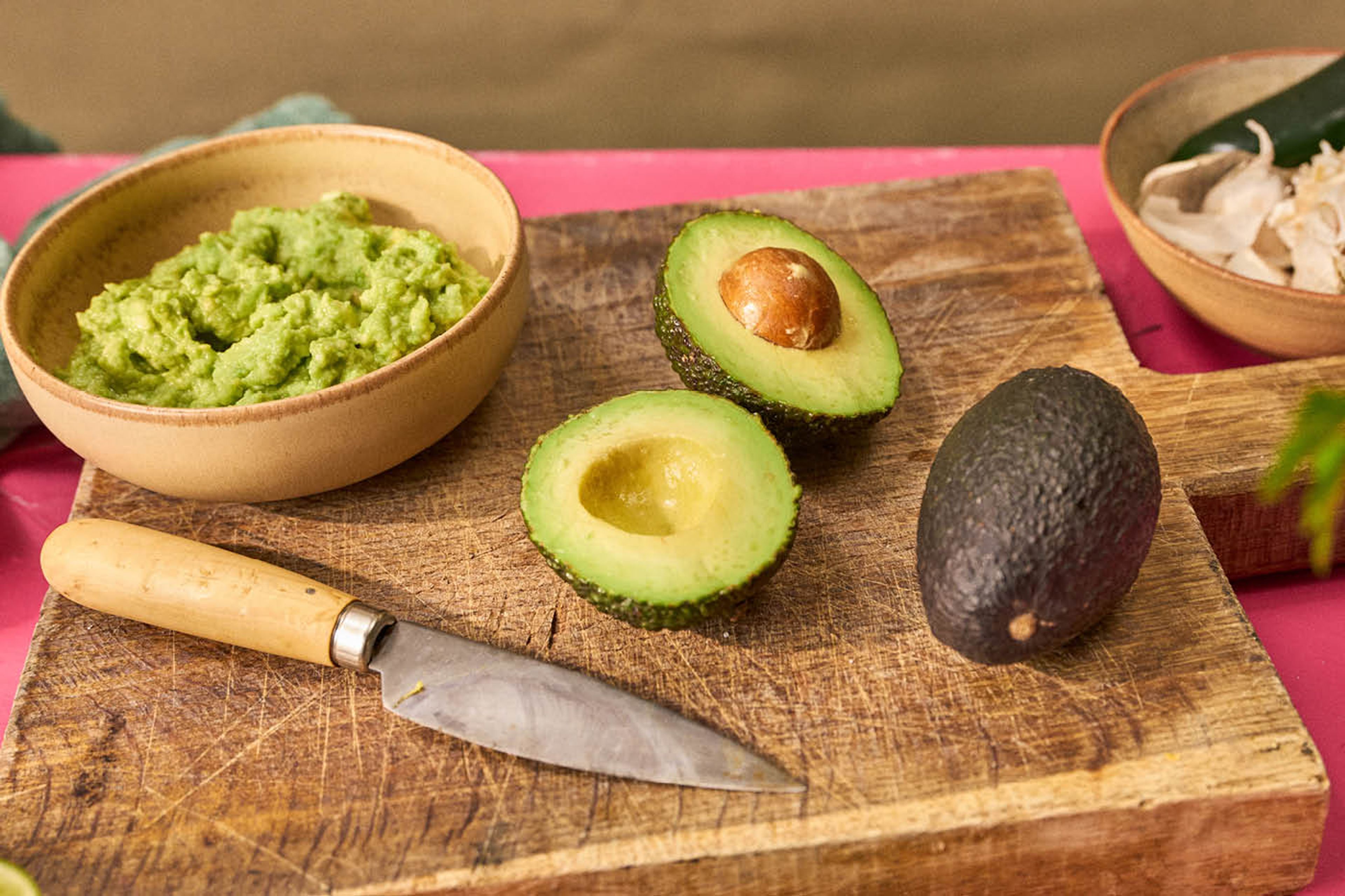 Skærebræt med avocadohalvdele og en skål med guacamole.