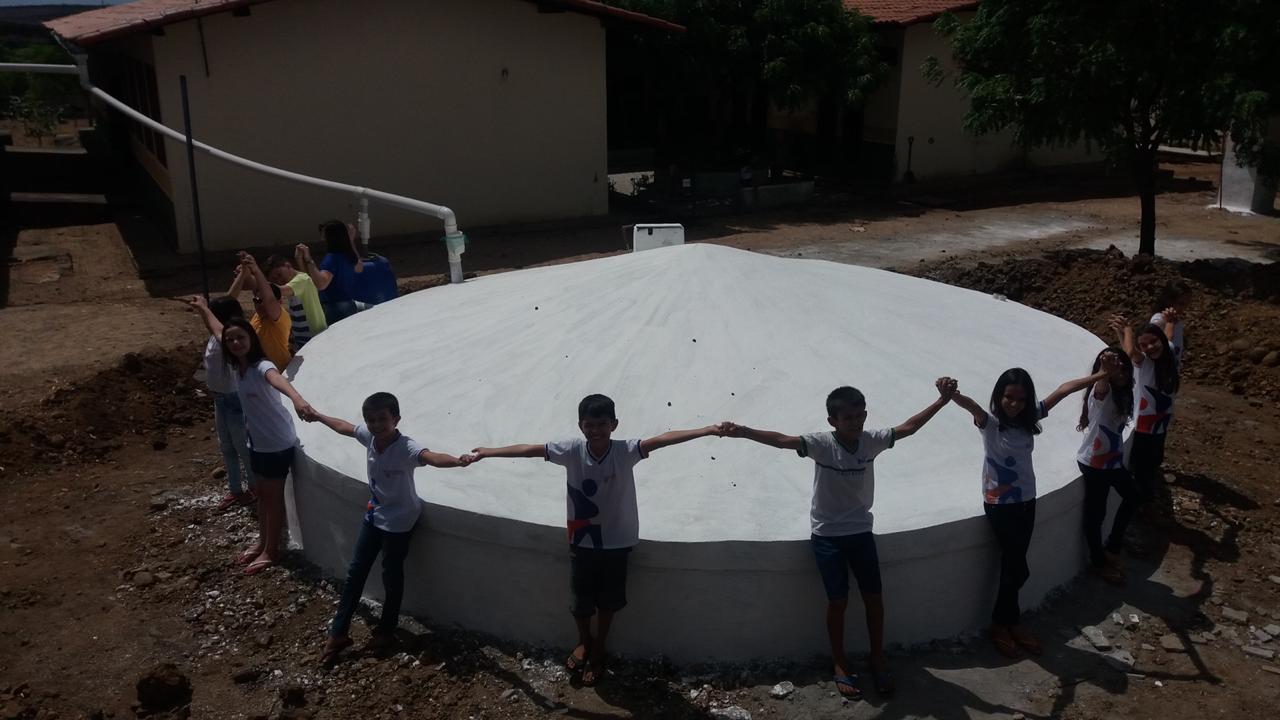 Crianças de mãos dadas em volta de uma cisterna escolar