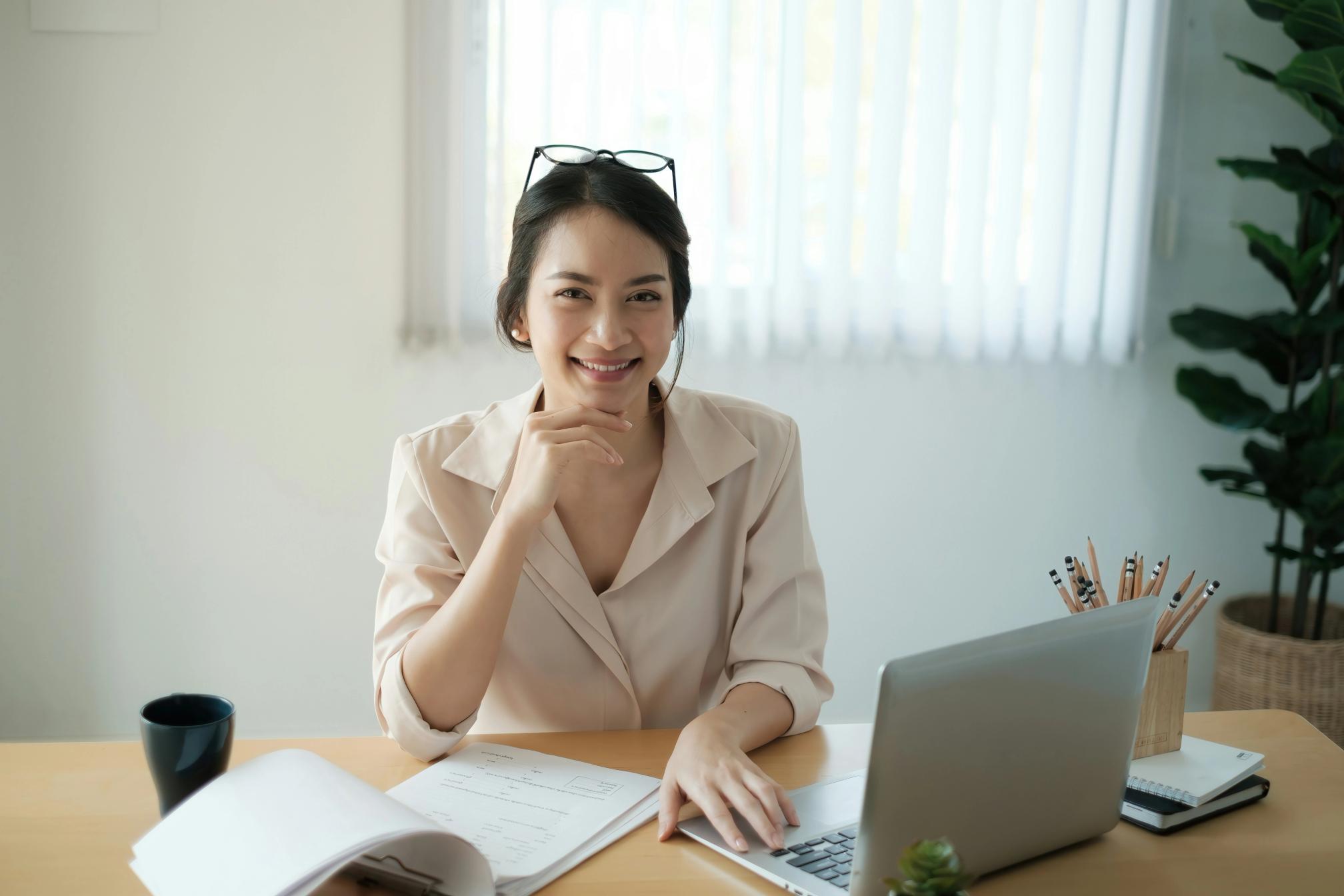 Young woman smiling with a laptop and paper in front of her on a wooden desk