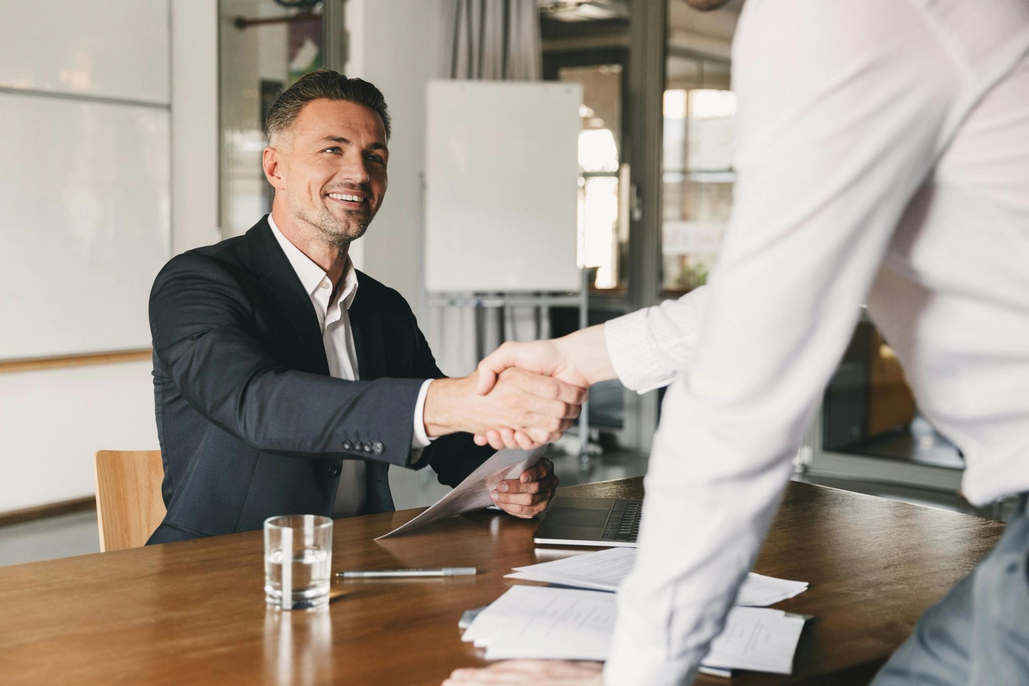 A man shaking hands with another man over a desk.