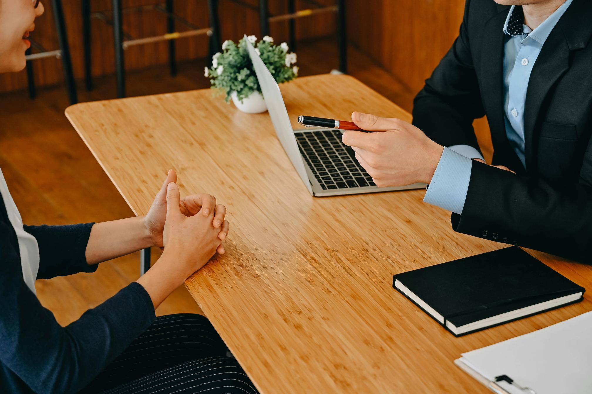 A man in a suit with a pen and a laptop interviewing a woman