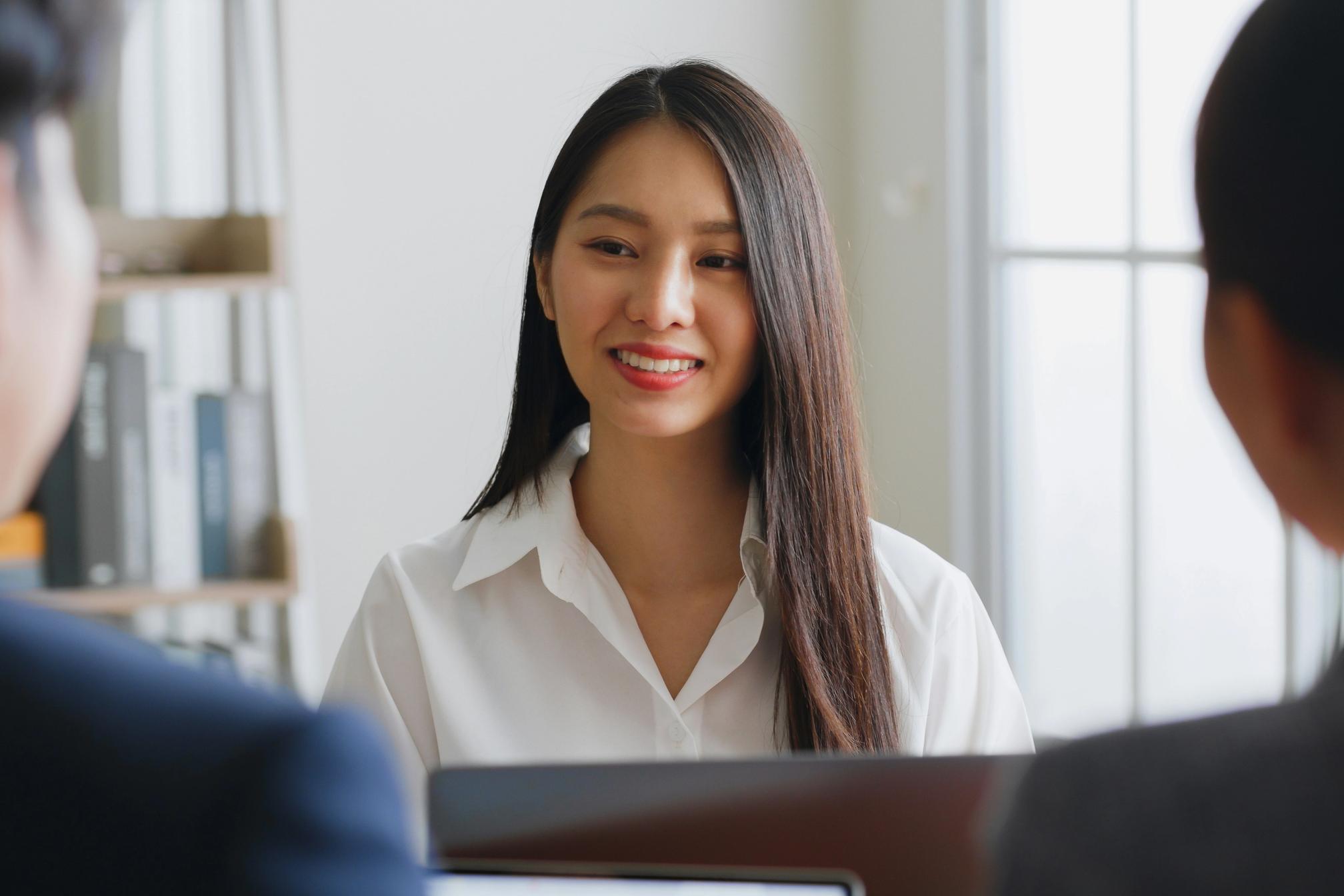A young woman with brown hair in business attire smiling during a job interview