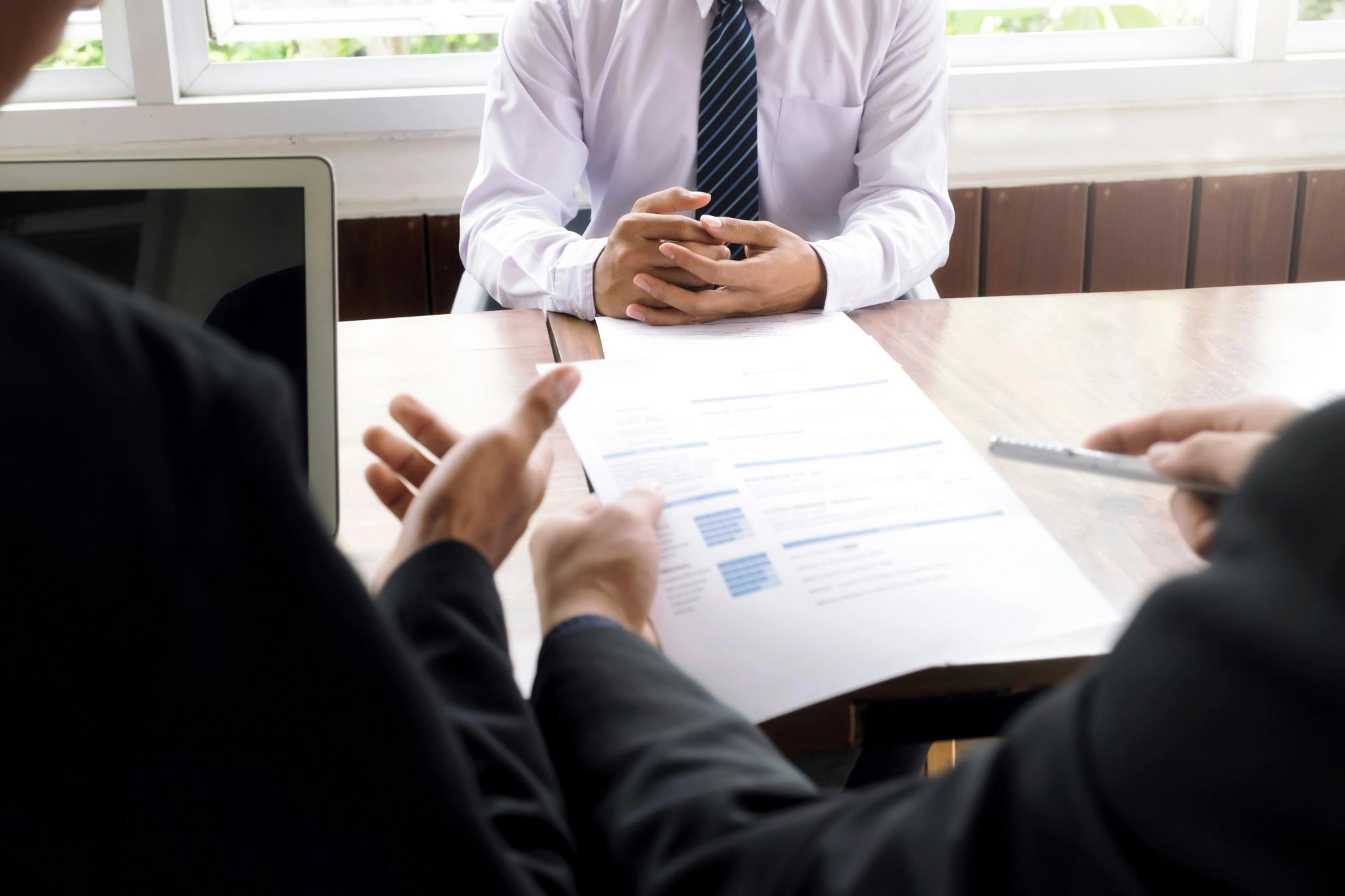A man in a white shirt and tie being interviewed by a man holding a resume and pen