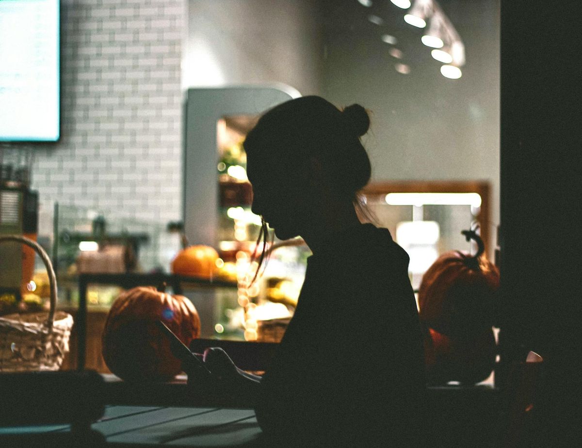 A woman's silhouette using her phone against a warm cafe backdrop in the evening.