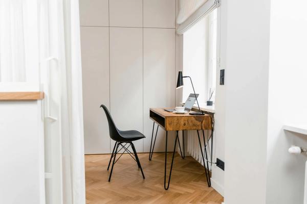 A minimalist home office corner with a wooden desk, a laptop, and a black chair.