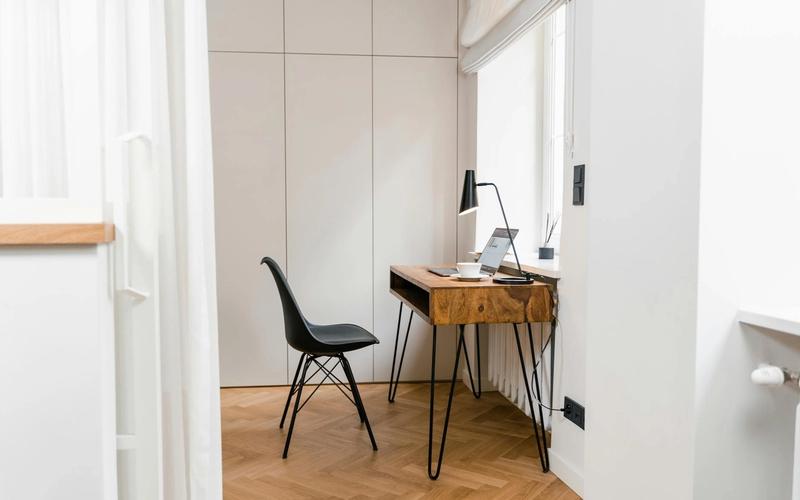 A minimalist home office corner with a wooden desk, a laptop, and a black chair.