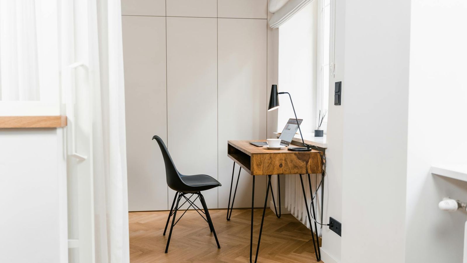 A minimalist home office corner with a wooden desk, a laptop, and a black chair.