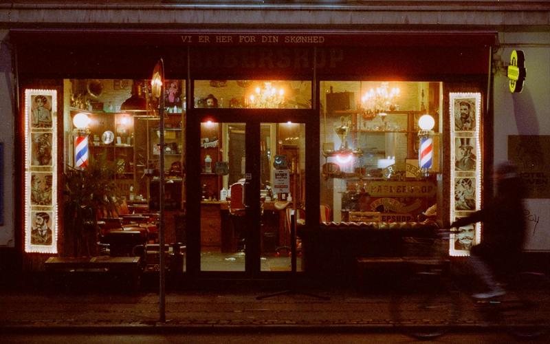 Warmly lit Copenhagen barbershop entrance at night with vintage signage.