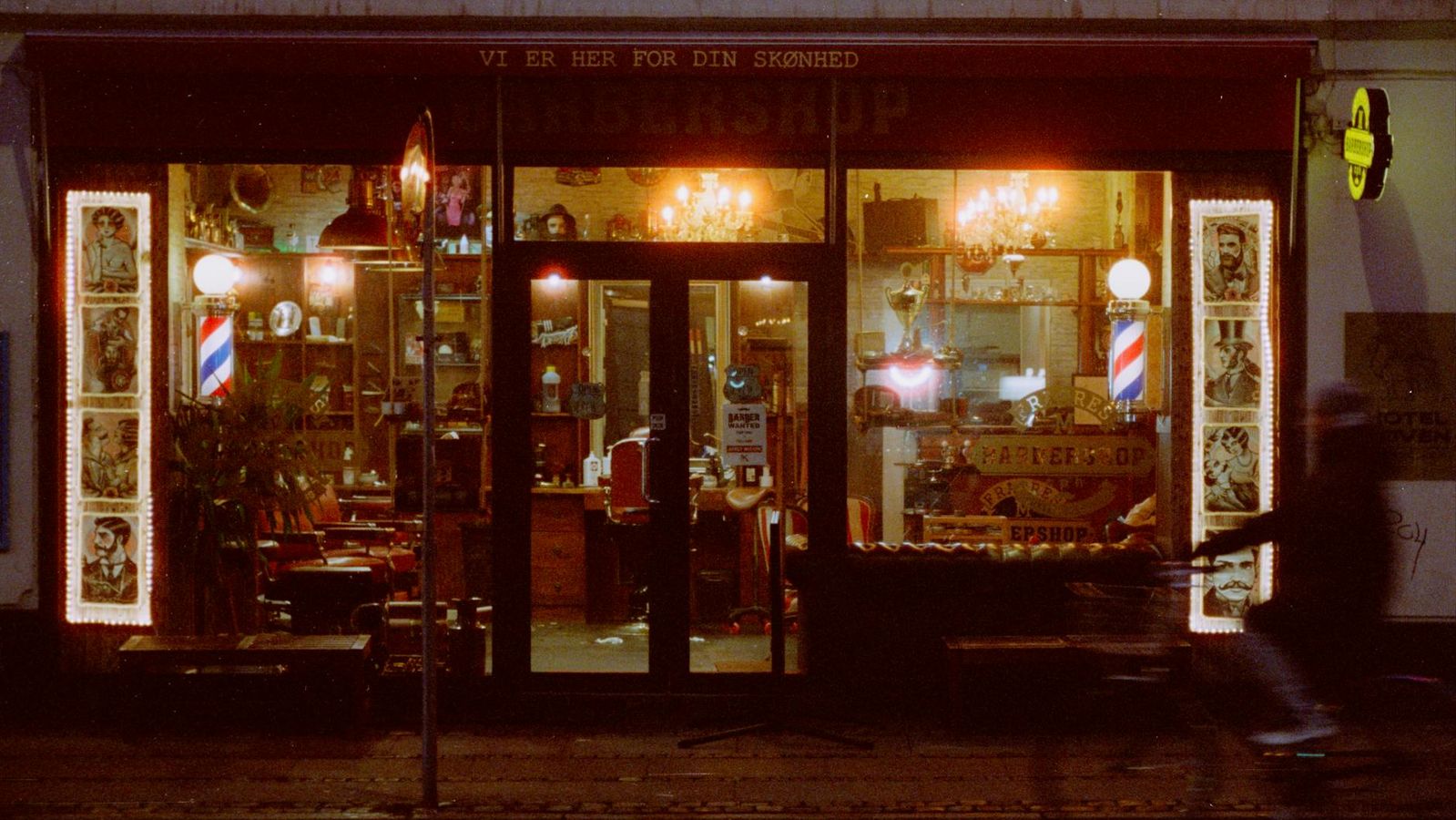 Warmly lit Copenhagen barbershop entrance at night with vintage signage.
