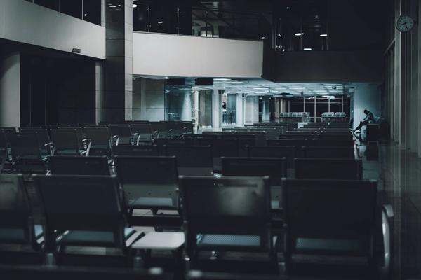 A dimly lit airport waiting area with empty rows and a lone figure in the distance.