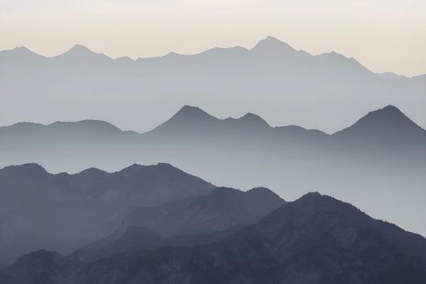 Mountain ridges in receding layers, fading into mist under a pale morning sky.
