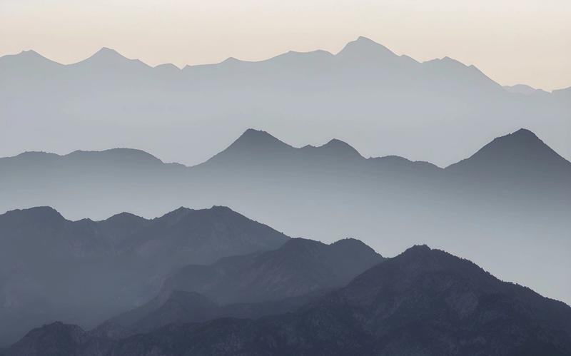 Mountain ridges in receding layers, fading into mist under a pale morning sky.