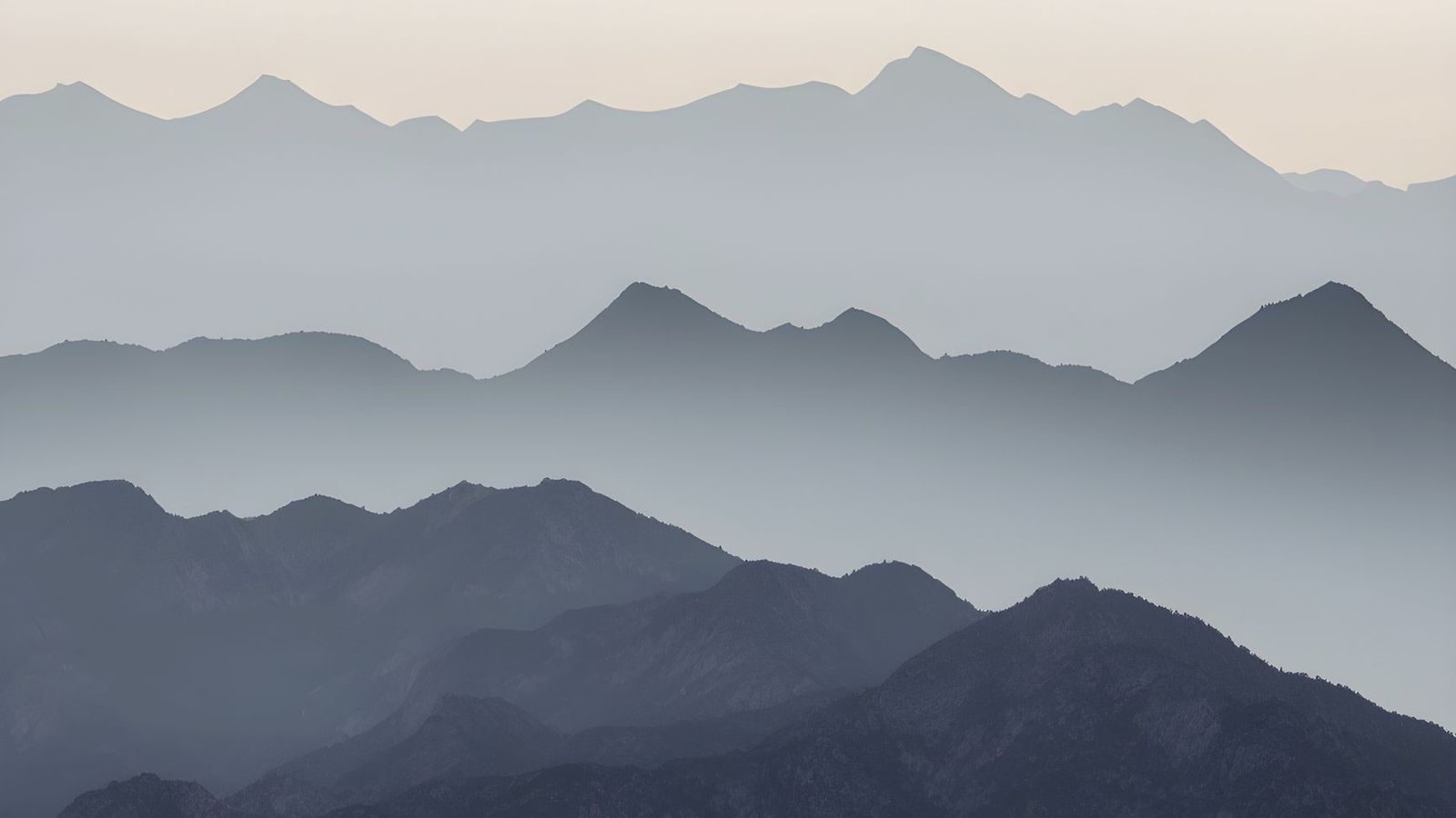 Mountain ridges in receding layers, fading into mist under a pale morning sky.