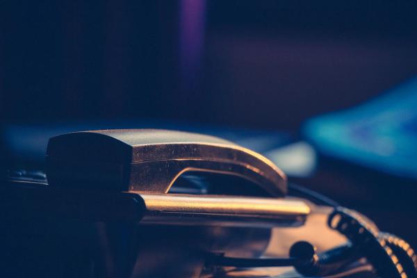 Close up of a telephone handset resting in its cradle, lit by warm light against a dark blue background.