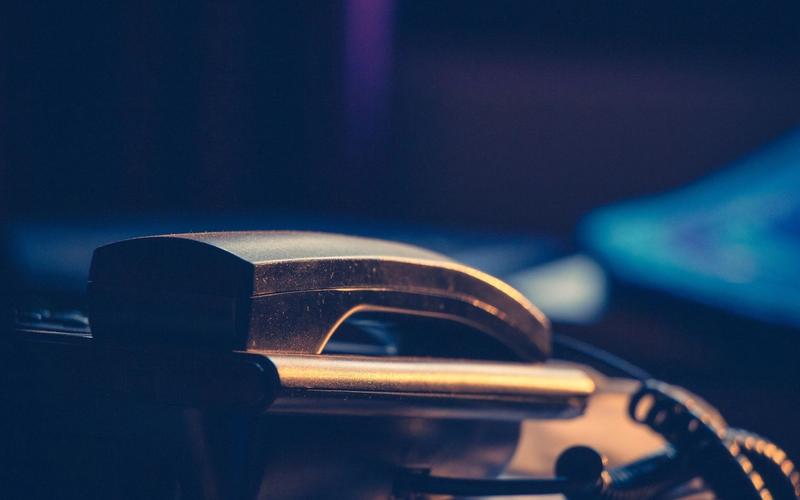 Close up of a telephone handset resting in its cradle, lit by warm light against a dark blue background.
